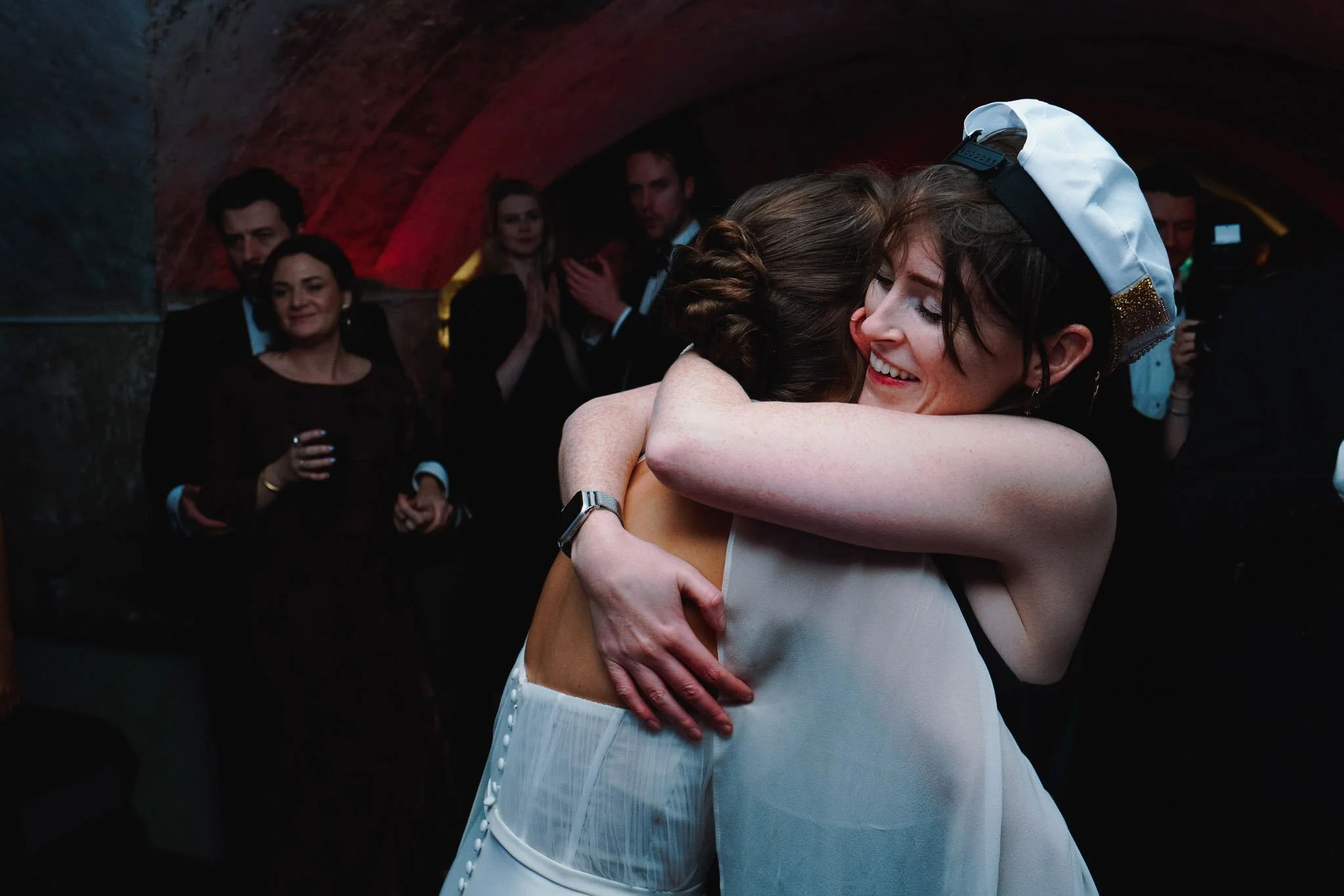 Bride and friend in a Tux Fizz sailor captain hat embrace on the dancefloor at the Crypts in the Mount Without in Bristol