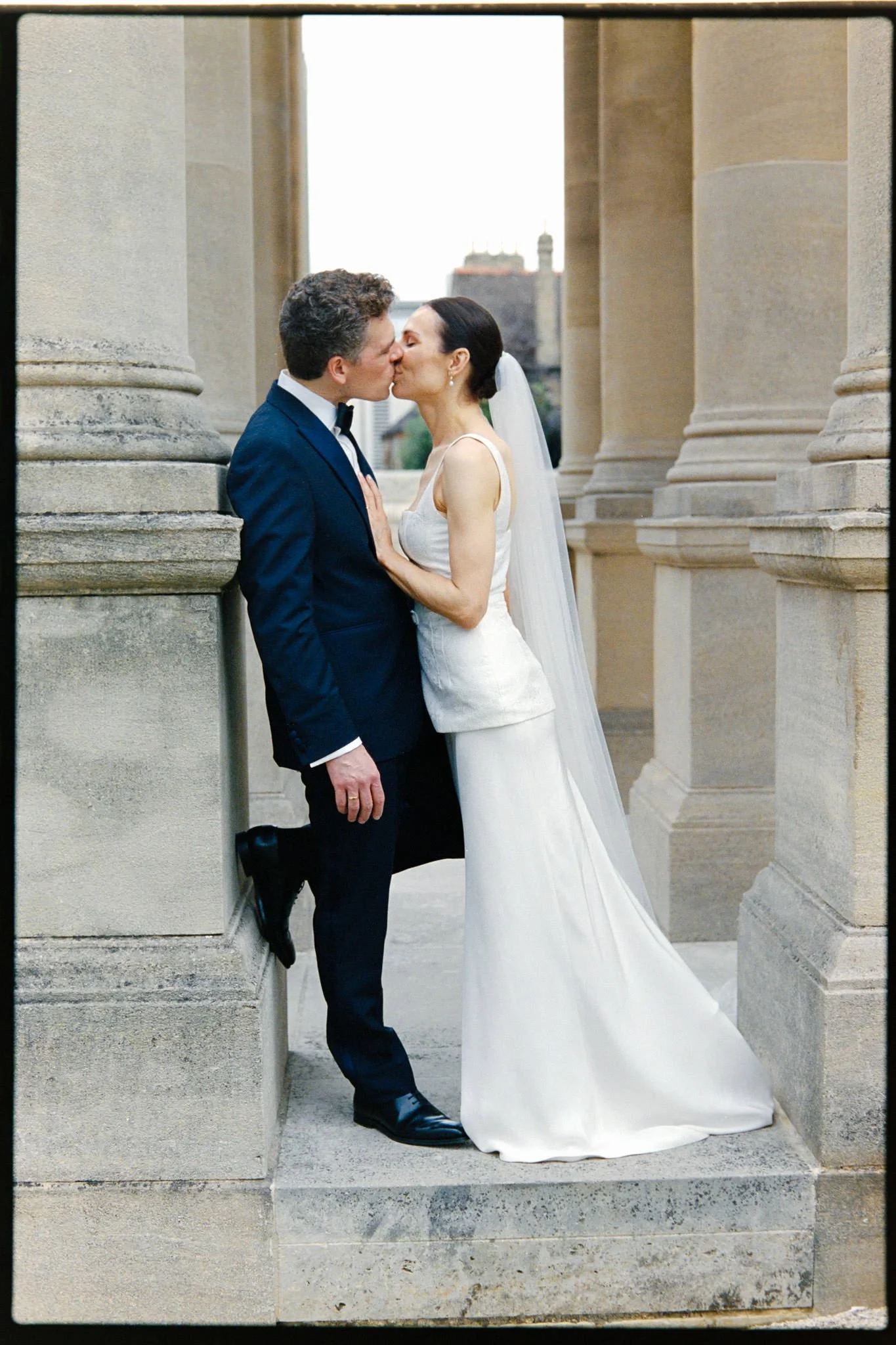 Wedding couple kissing between pillars in Oxford.