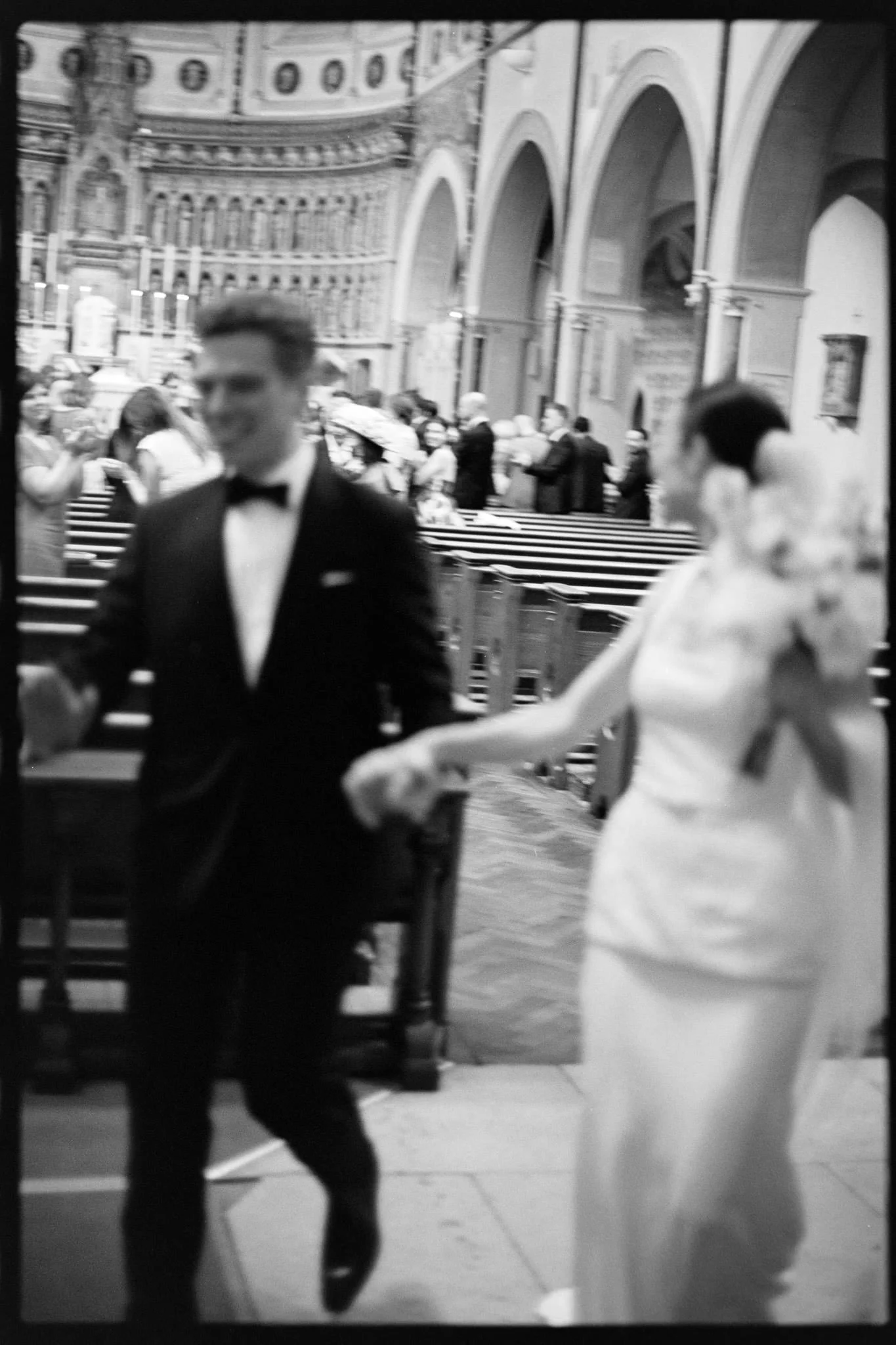 A couple leave the church in black and white on film with slow shutter blur