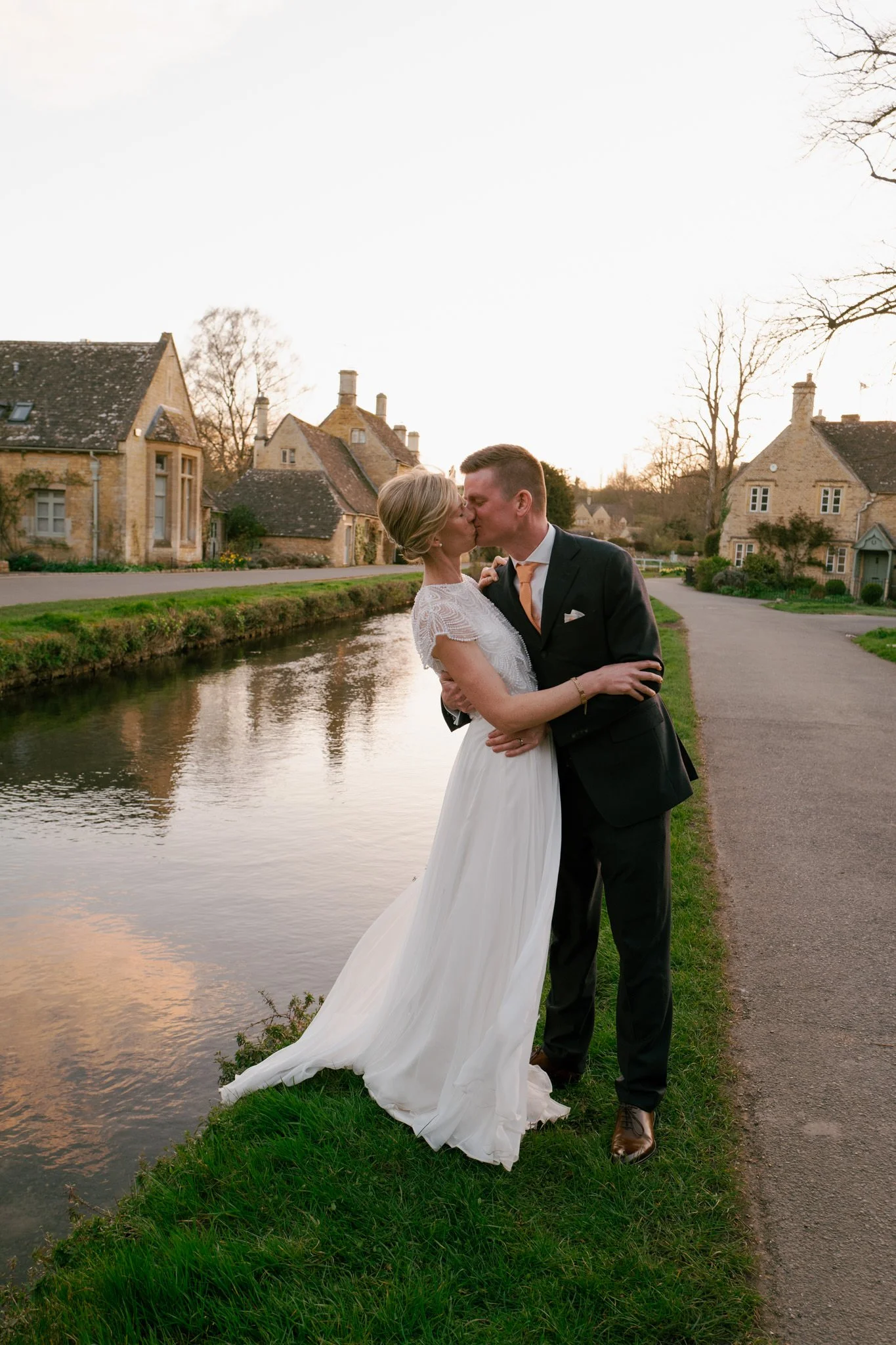 Bride and groom kissing at sunset at Lower Slaughter in the cotswolds by a steam in the village