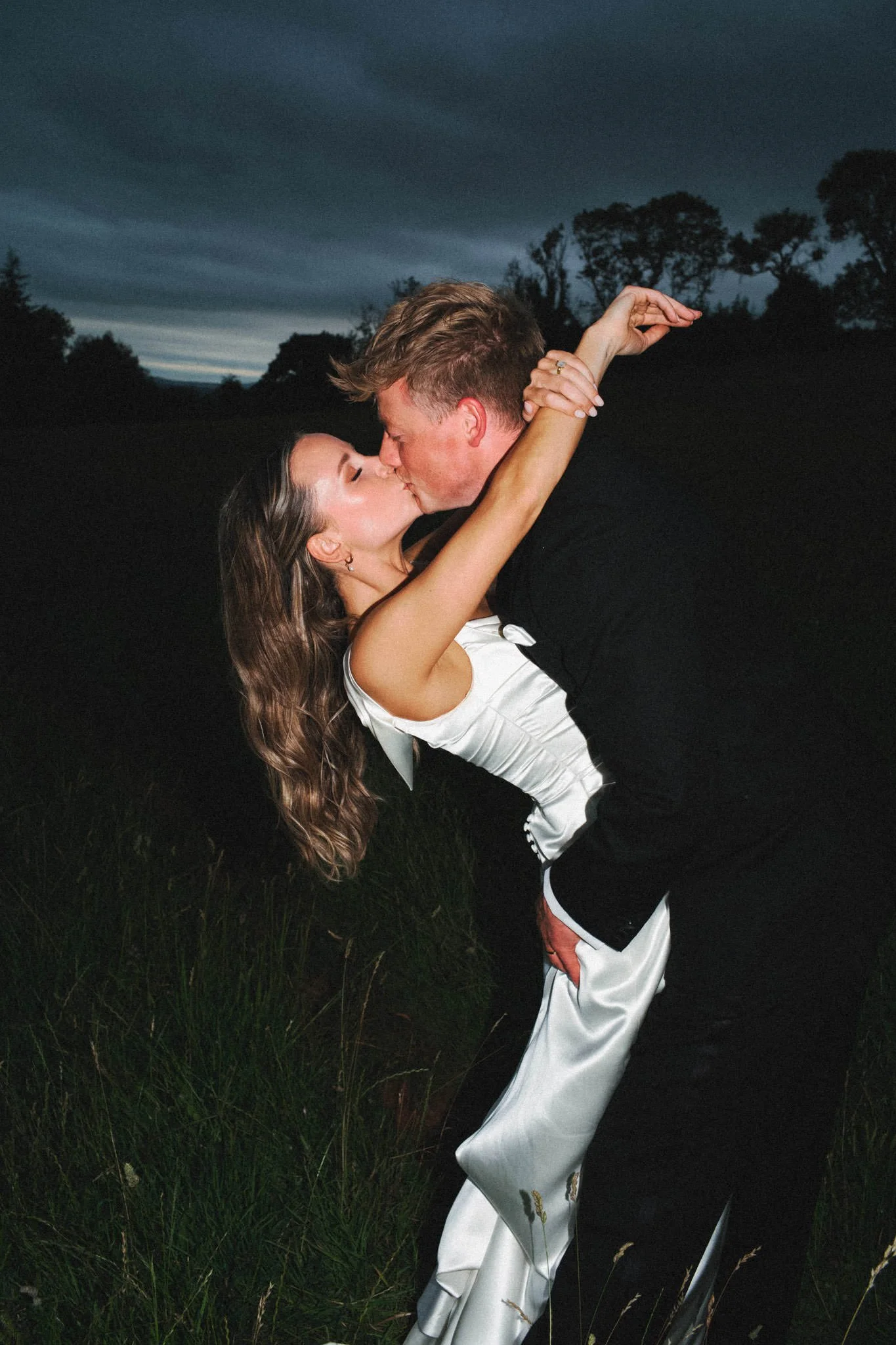 Bride leans backwards as she kisses the groom with her arms around his neck with direct front flash just outside Bristol