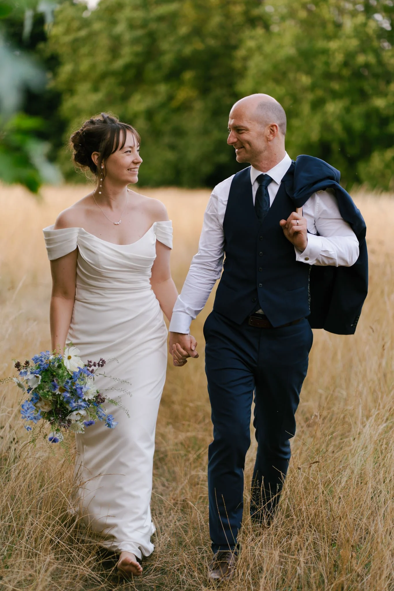 Bride and groom walk through summer grass at their wedding