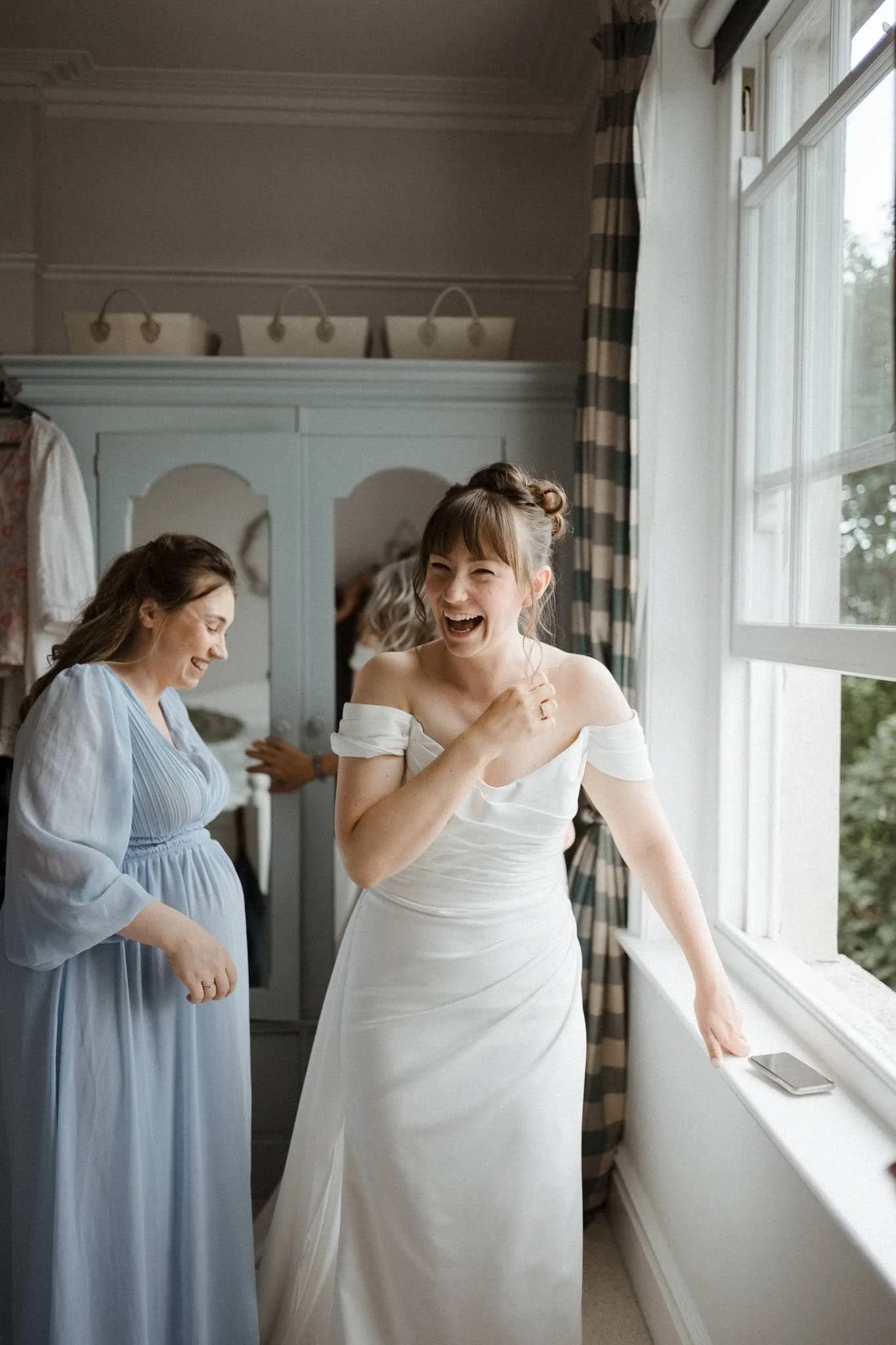 A bride laughing by a window while she gets ready for her wedding in Bristol