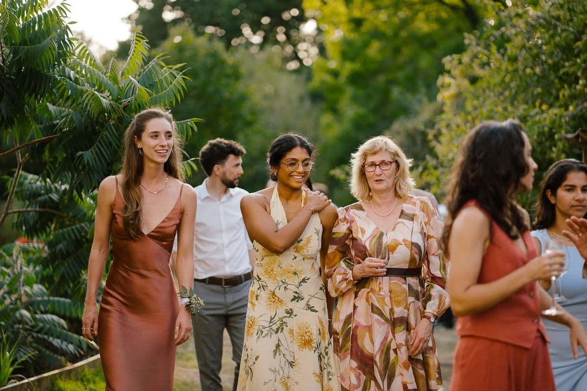 A diverse group of wedding guests walk together at sunset among palm fronds at Folly Farm, Bristol — a warm, golden-hour colour wedding photo