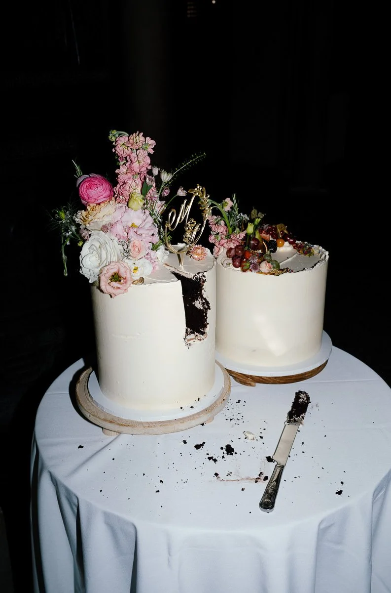 Bold direct-flash shot of a wedding cake with the first slice cut, dramatic black background and strong colour contrast