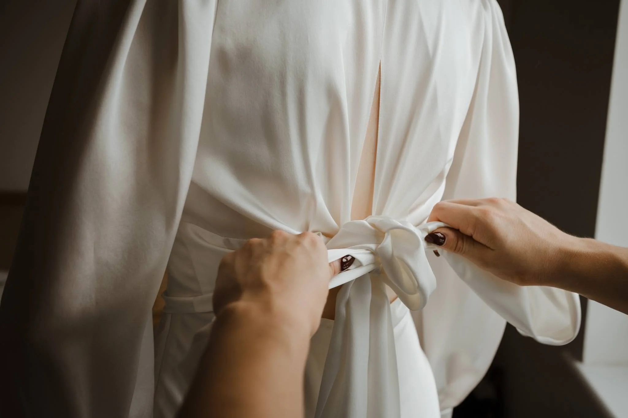 Photograph of hands tying the back of the dress at a London Wedding