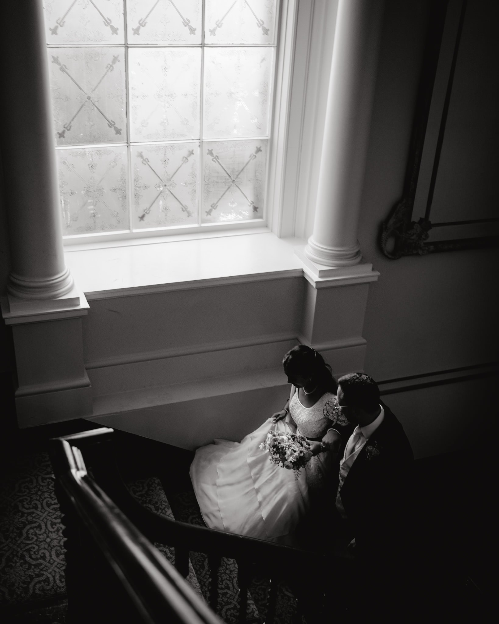 Bride and groom climb the stairs at Hensol Castle by a big window