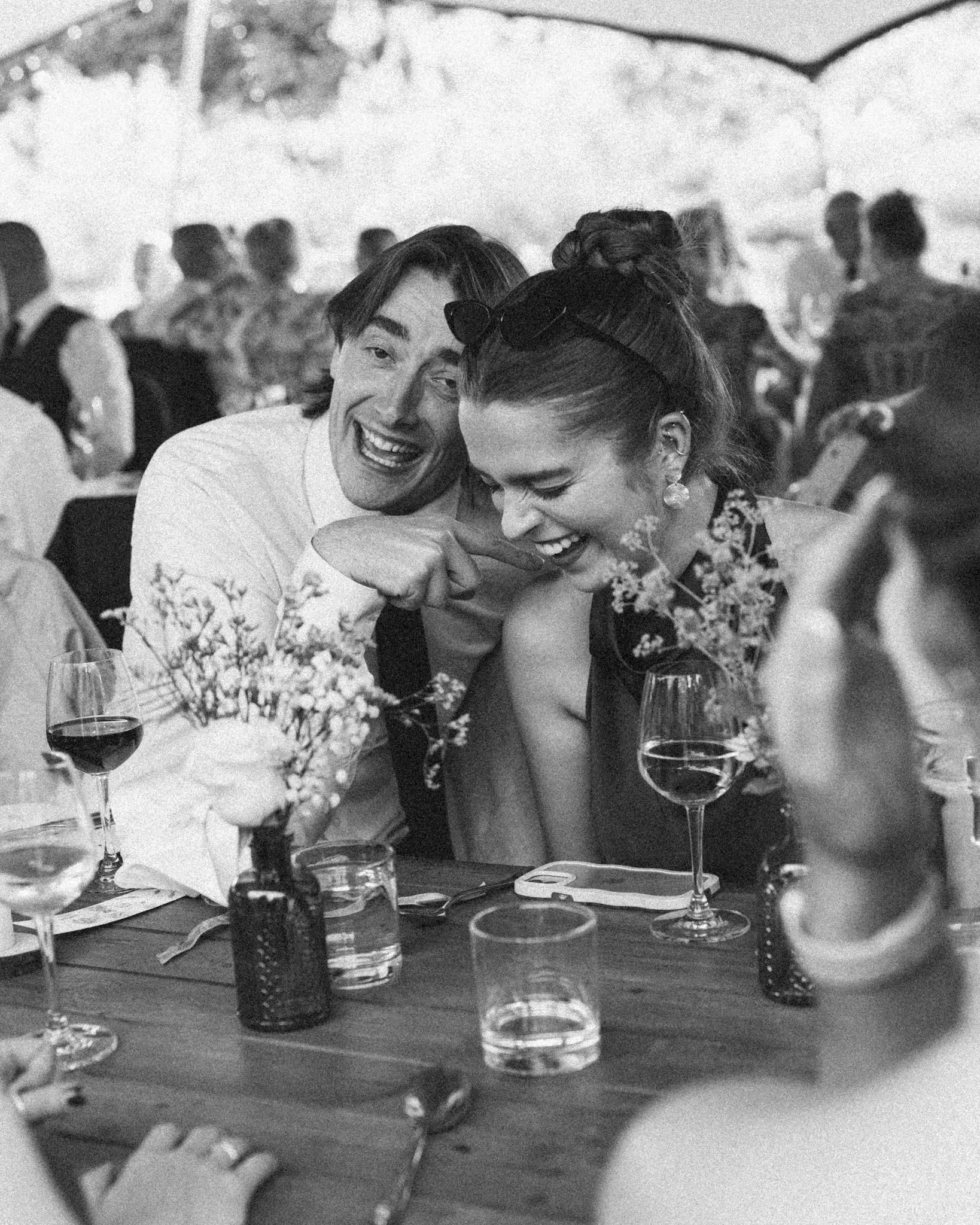 A couple bent over in hysterics during speeches at a wedding in Bristol in black and white on film