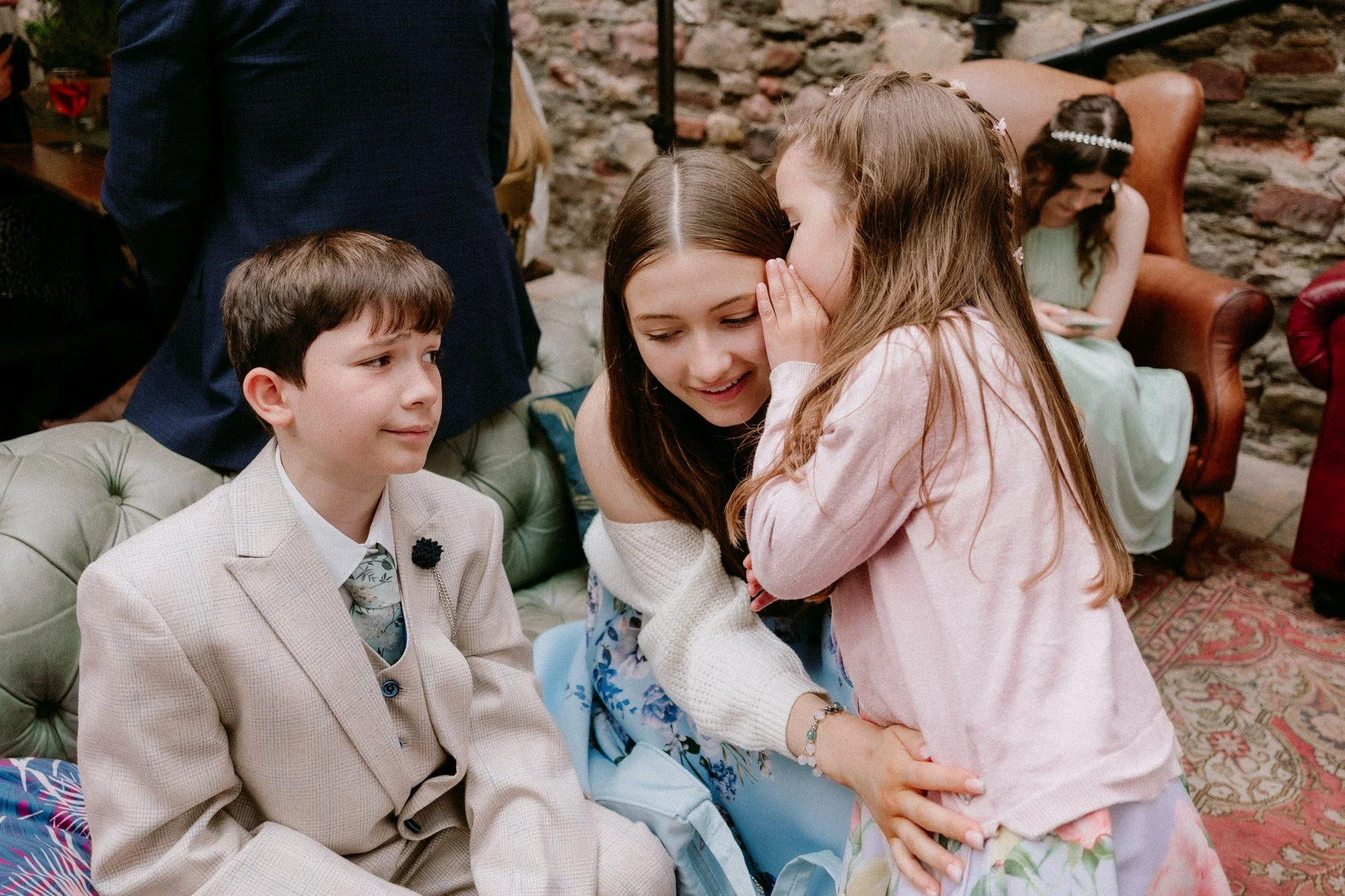 A little girl whispers to an older girl while a young boy looks on at a wedding in Bristol