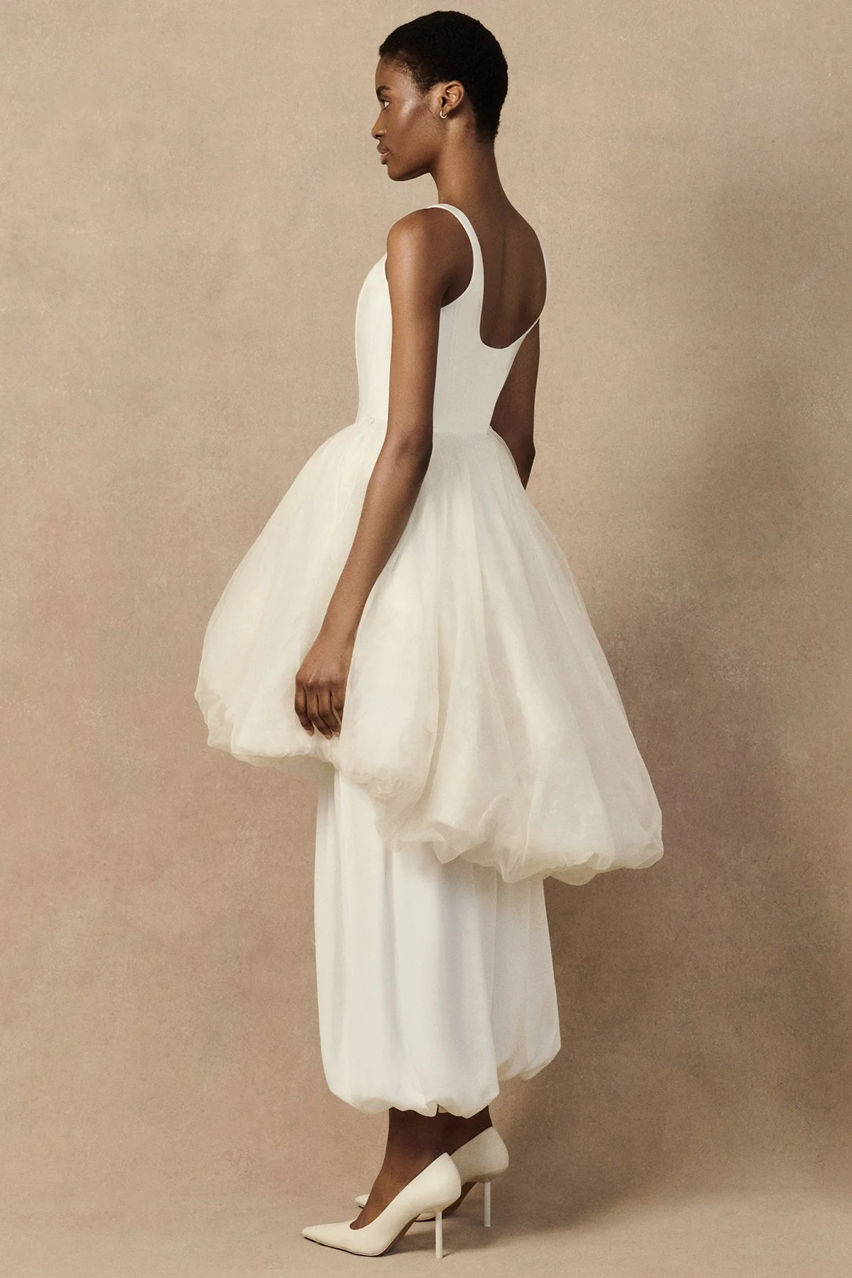 side image of Oxana bridal trouser in hammered crepe satin featuring graphic pleating, side slits, and elasticated ankle hems. Worn with Penelope corset and Meg mini