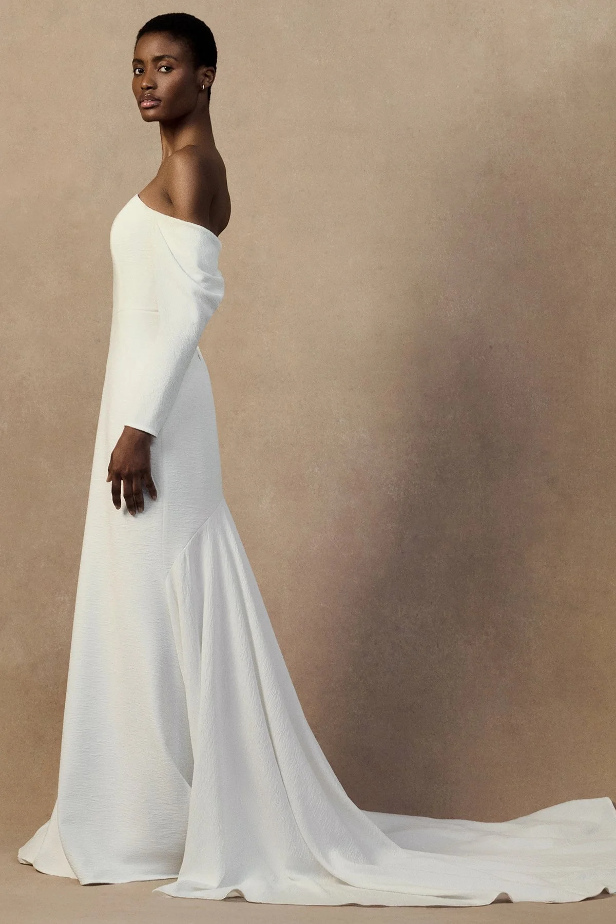 side image of white wedding gown nicole dress in plissé-textured cloqué featuring a curved upward neckline with draped long sleeves.