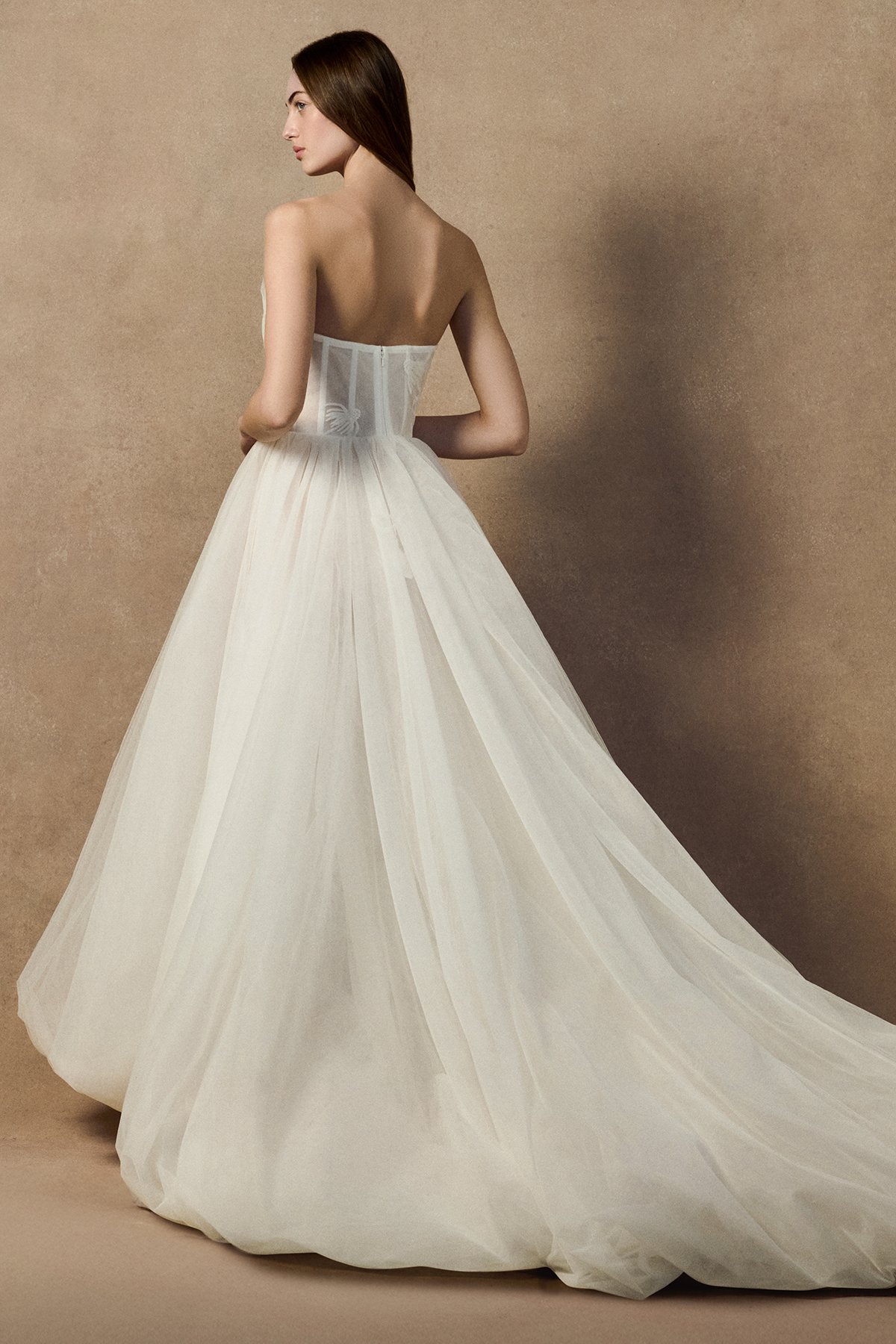 Back image of model wearing the Cosmos bridal dress with a sheer exposed corset, hand-stitched echinacea floral embroidery, and a voluminous bubble-hem tulle skirt.