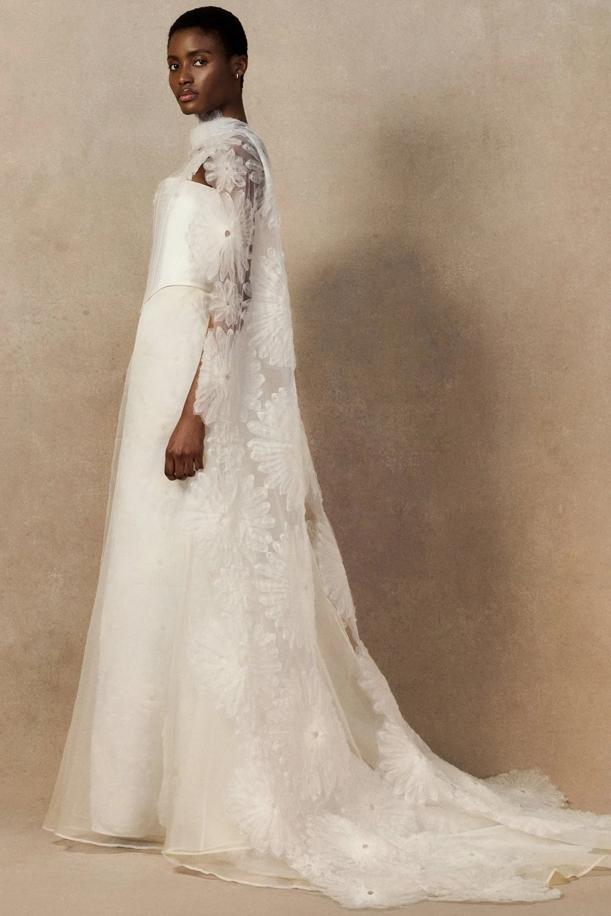 side image of Fig cape in sheer silk organza featuring hand-cut looped daisy motifs with raw-edged detailing worn over the décolletage