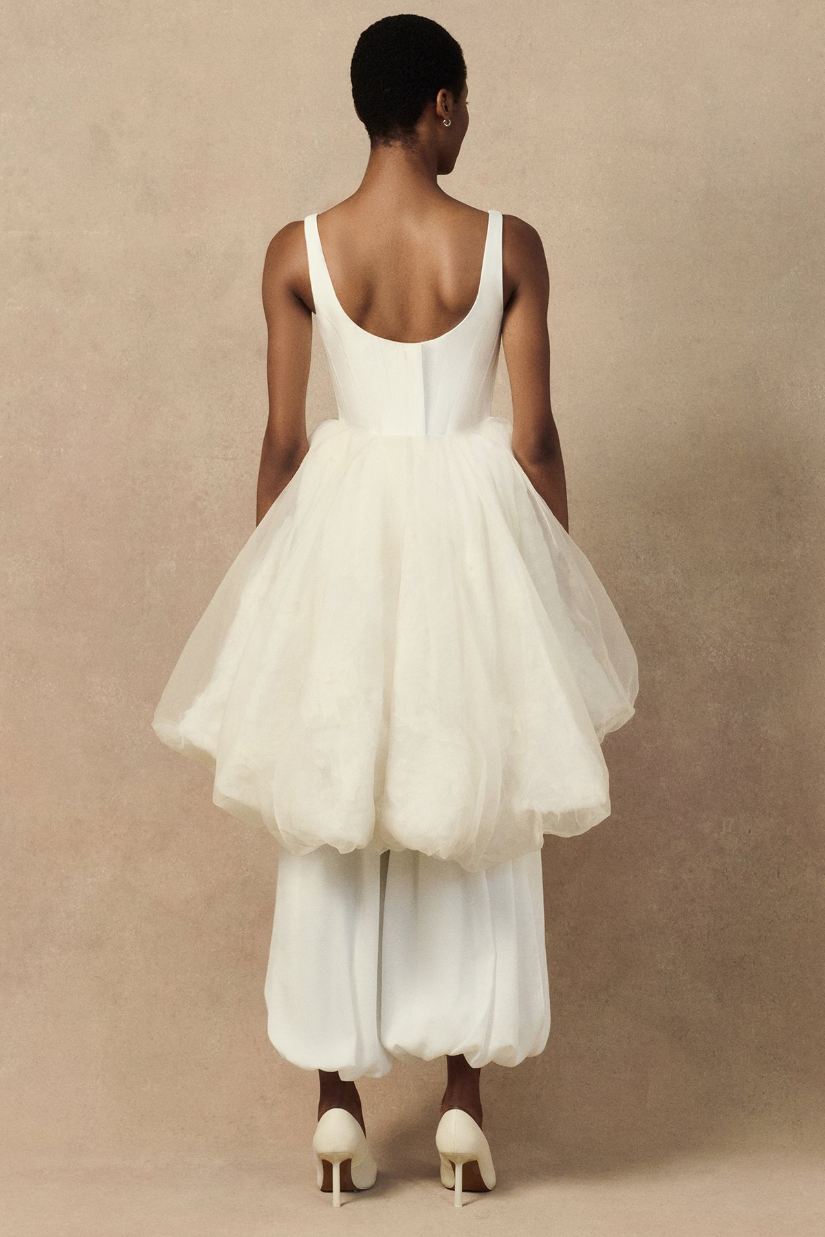 back image of Oxana bridal trouser in hammered crepe satin featuring graphic pleating, side slits, and elasticated ankle hems. Worn with Penelope corset and Meg mini skirt