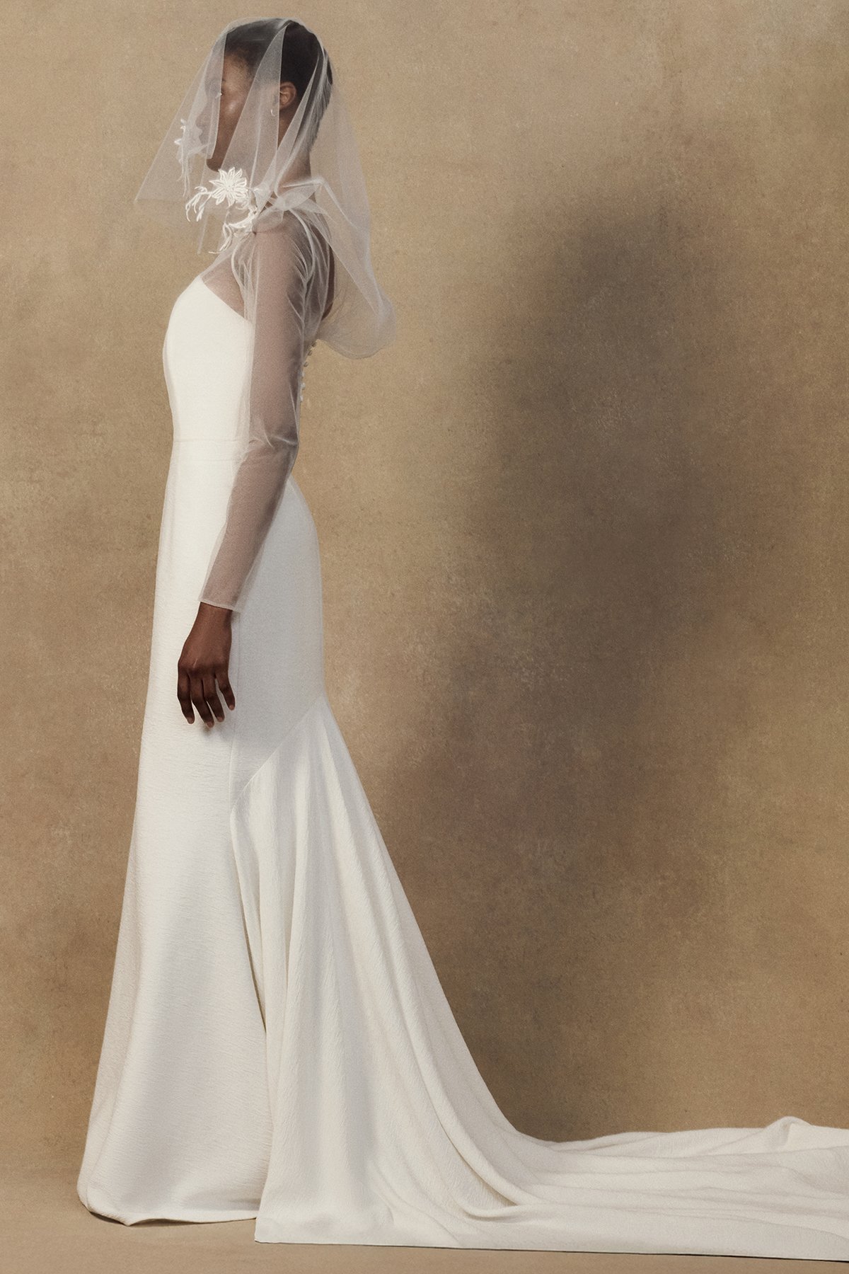 side image of sheer tulle Geum Jacket featuring a draped cowl back and a multifunctional hood that can be styled as a bridal veil. worn with strapless Nicole wedding gown