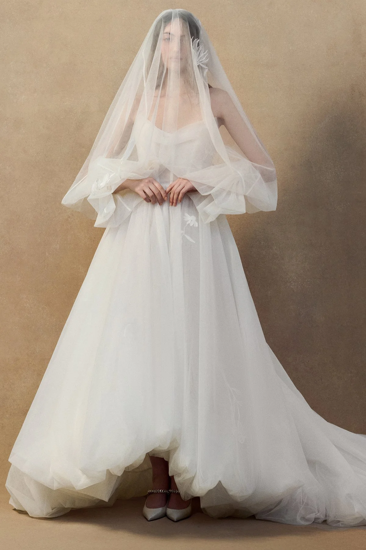 front images of the Kerry Veil in double-layered tulle with a voluminous sheer silhouette that drapes over the head and shoulders to gather at the wrist creating sleeves