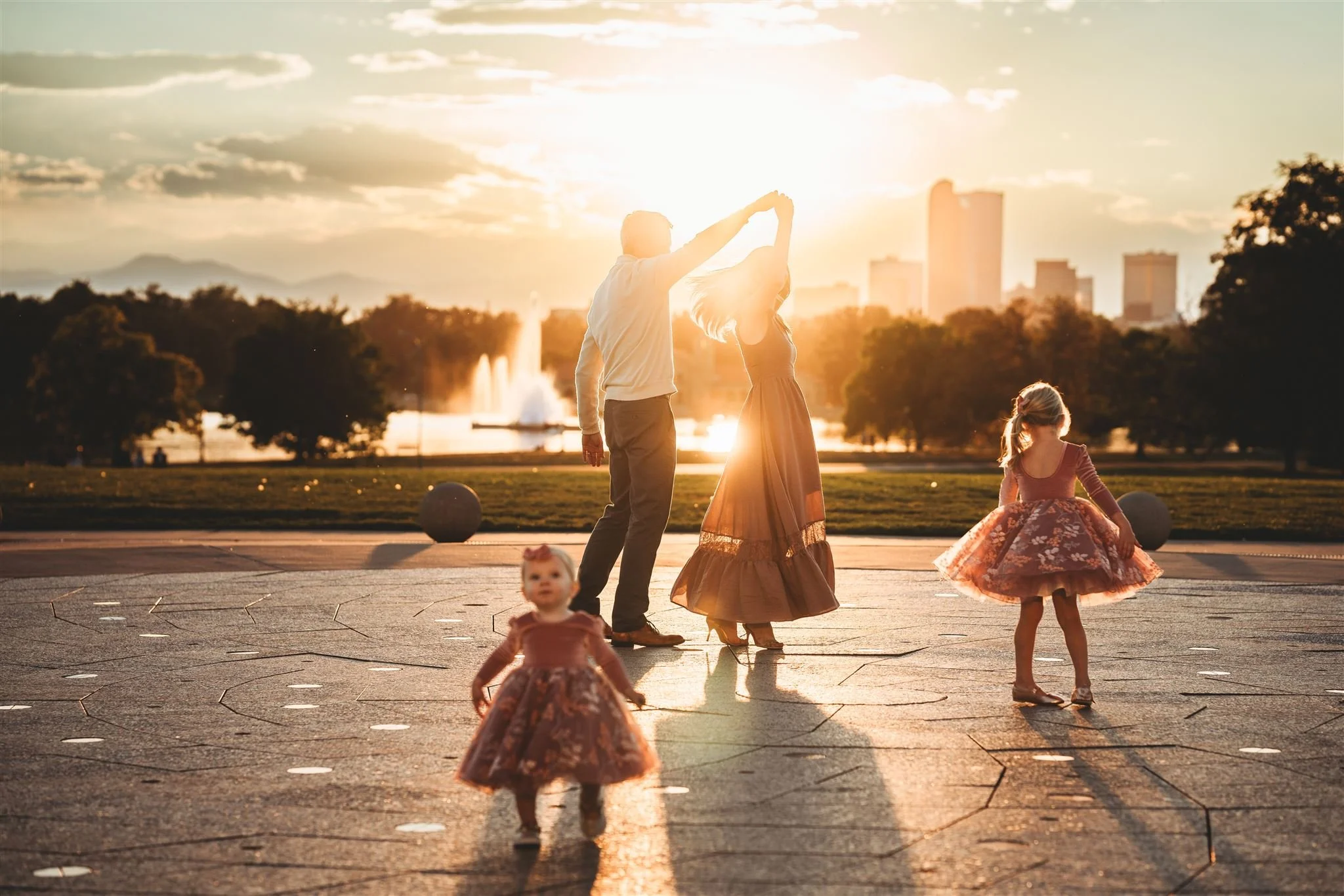 City Park Family Session in Denver| Family Dancing at City Park, Denver. The sun is setting. You can see the Denver skyline in the background.
