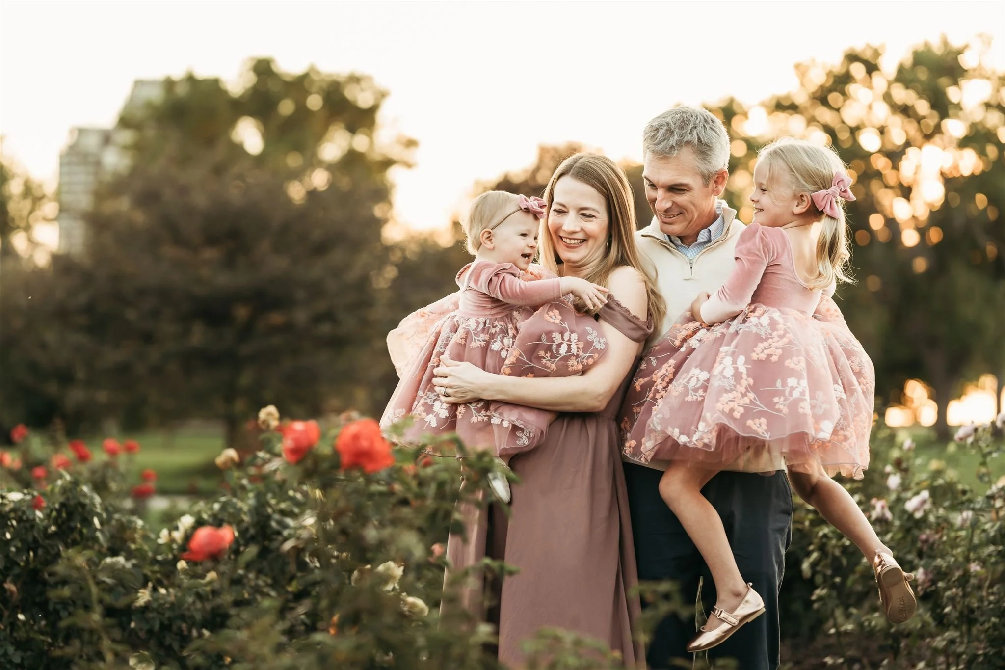 Denver Family Photographer | Mother and father hold two daughters in pink dresses in the rose garden at City Park in Denver