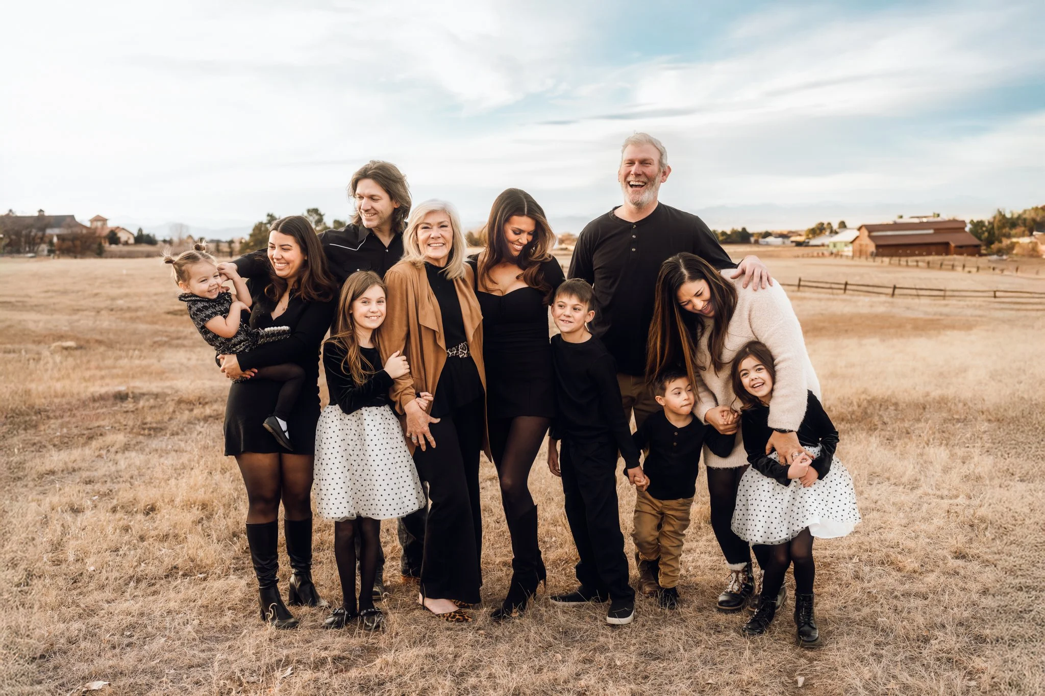 Boulder Extended Family Session | Family stands together in a field, smliing and looking at one another.