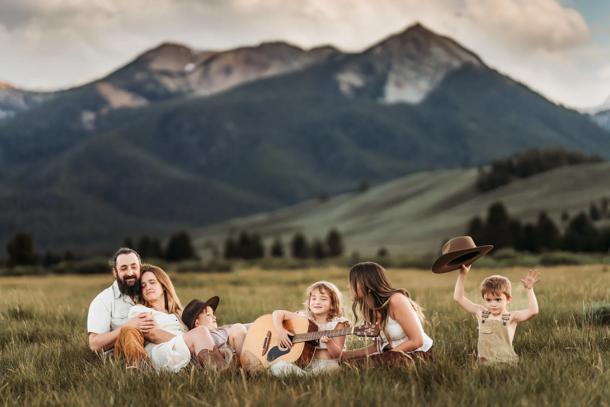 Best Camera For Family Photography | Family sitting on grass with mountains in background, child holding guitar.