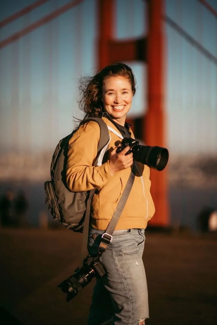 Best Photo Gear for Family Photographers. Jill Slagter standing with camera smiling in front of the Golden Gate Bridge.