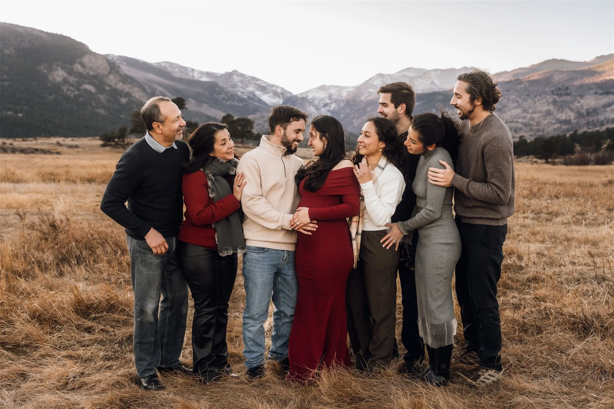 Multi-generation family photos in Rocky Mountain National Park | Family gathers around a couple, all looking at them looking at each other. The woman is pregnant.