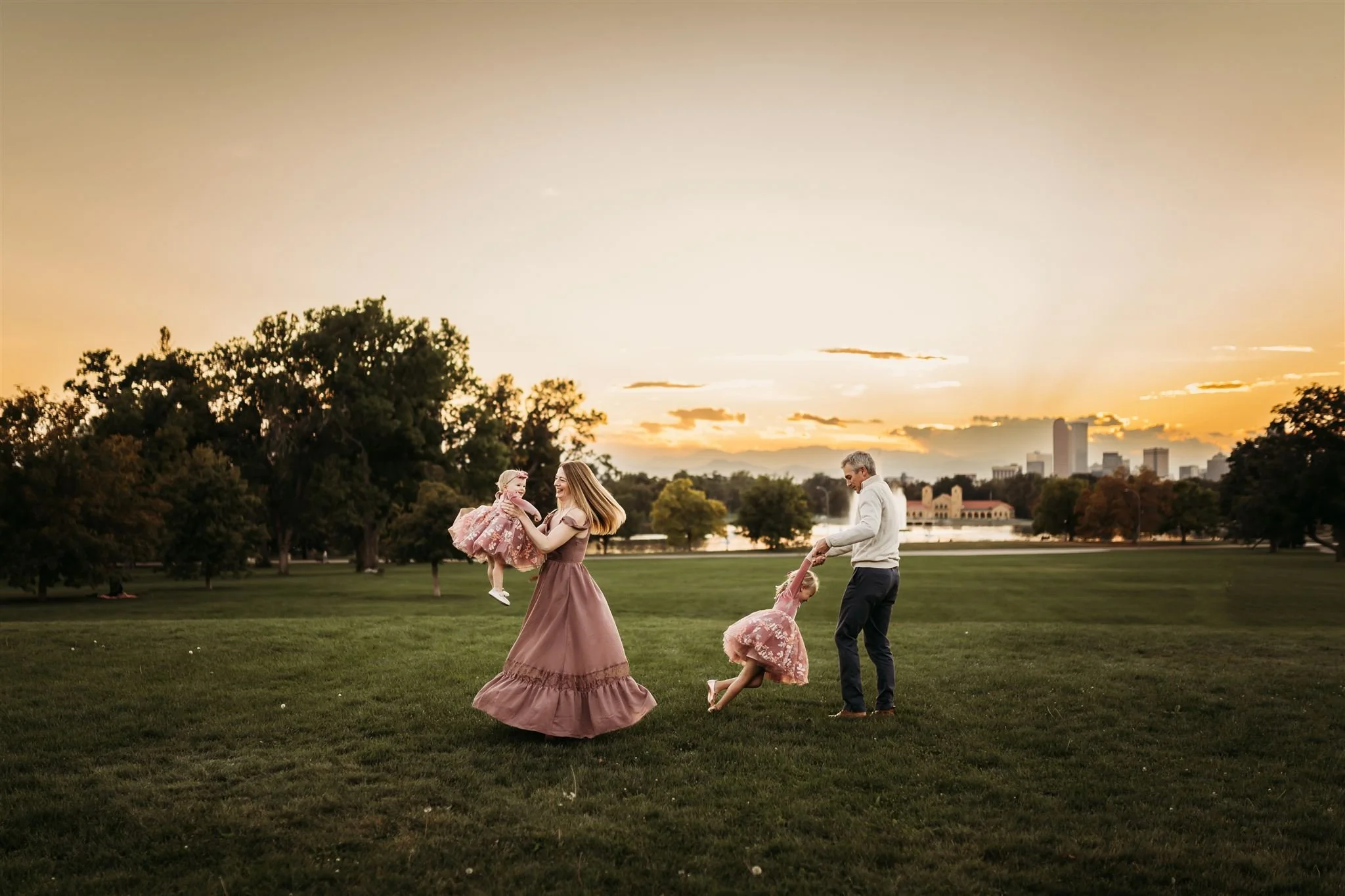 Denver Family Photographer | Mother and father dance with two girls in pink dresses in the lawn at City Park in Denver.