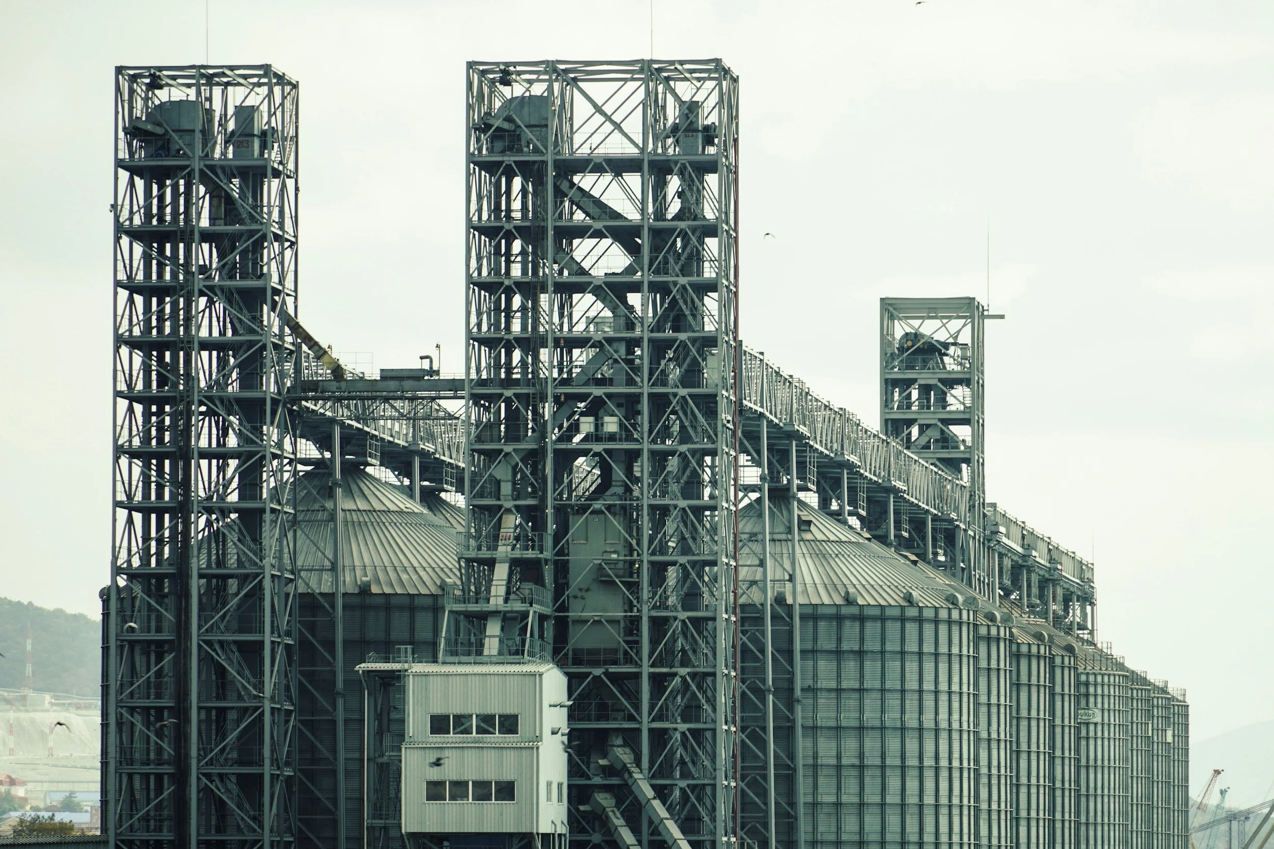 Industrial building with metal framework, staircases, and ventilation structures, under a cloudy sky.