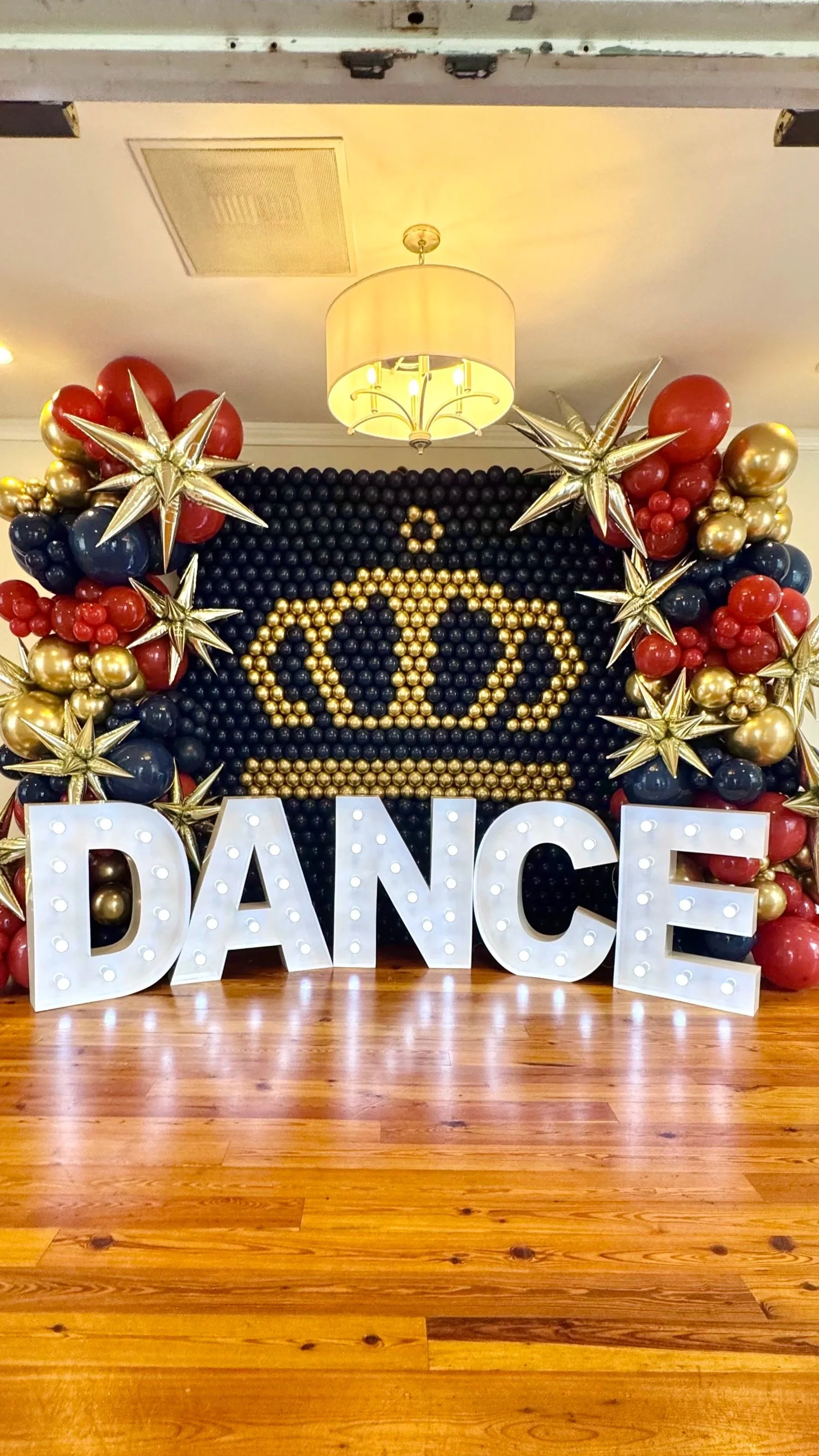 Balloon backdrop with a golden crown design and the word 'DANCE' spelled out in large marquee letters, decorated with gold, red, and black balloons and star-shaped balloons.