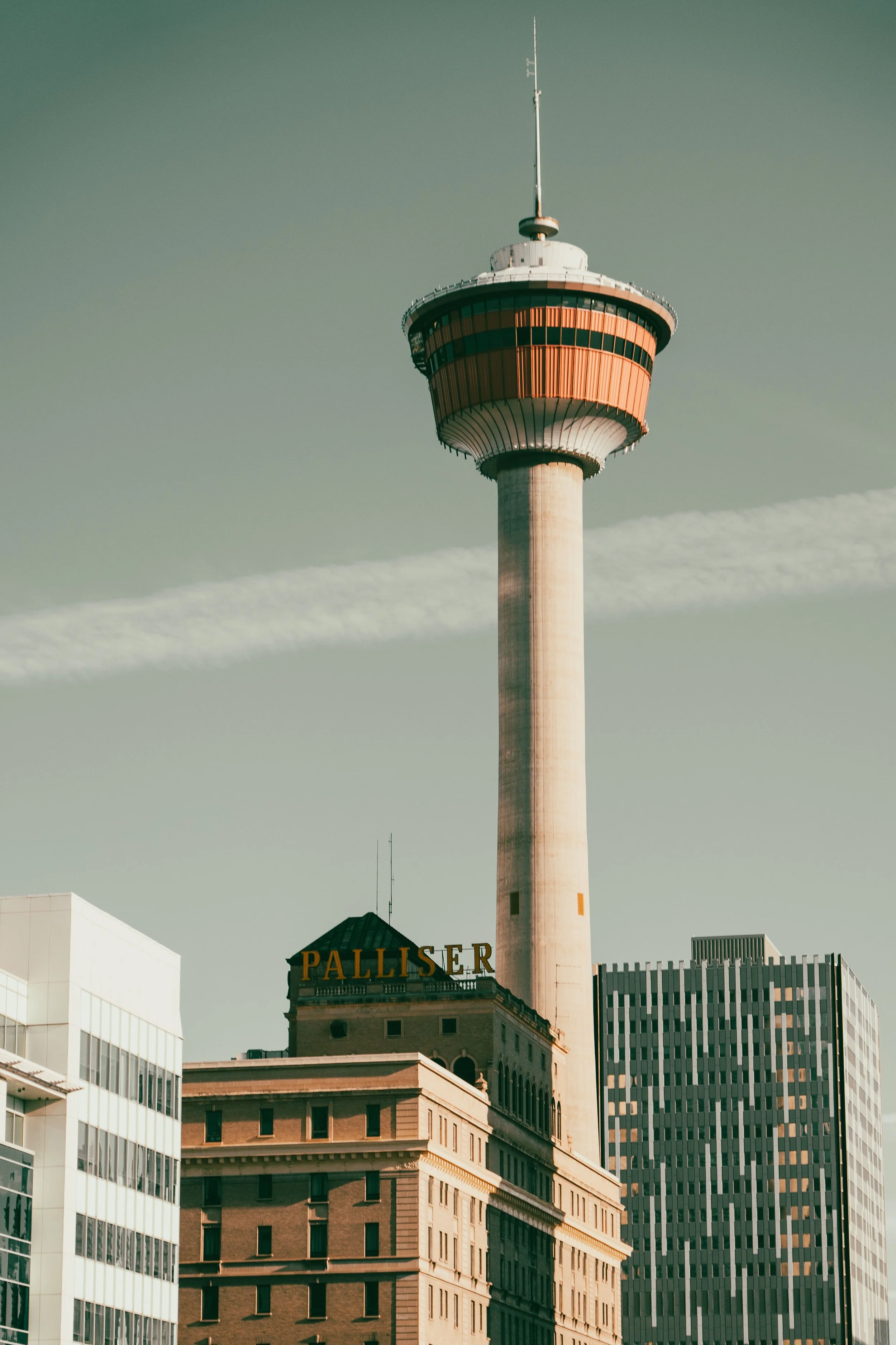 A cityscape with tall buildings, including a prominent communication tower with a large round observation deck near the top, against a sky with light clouds.