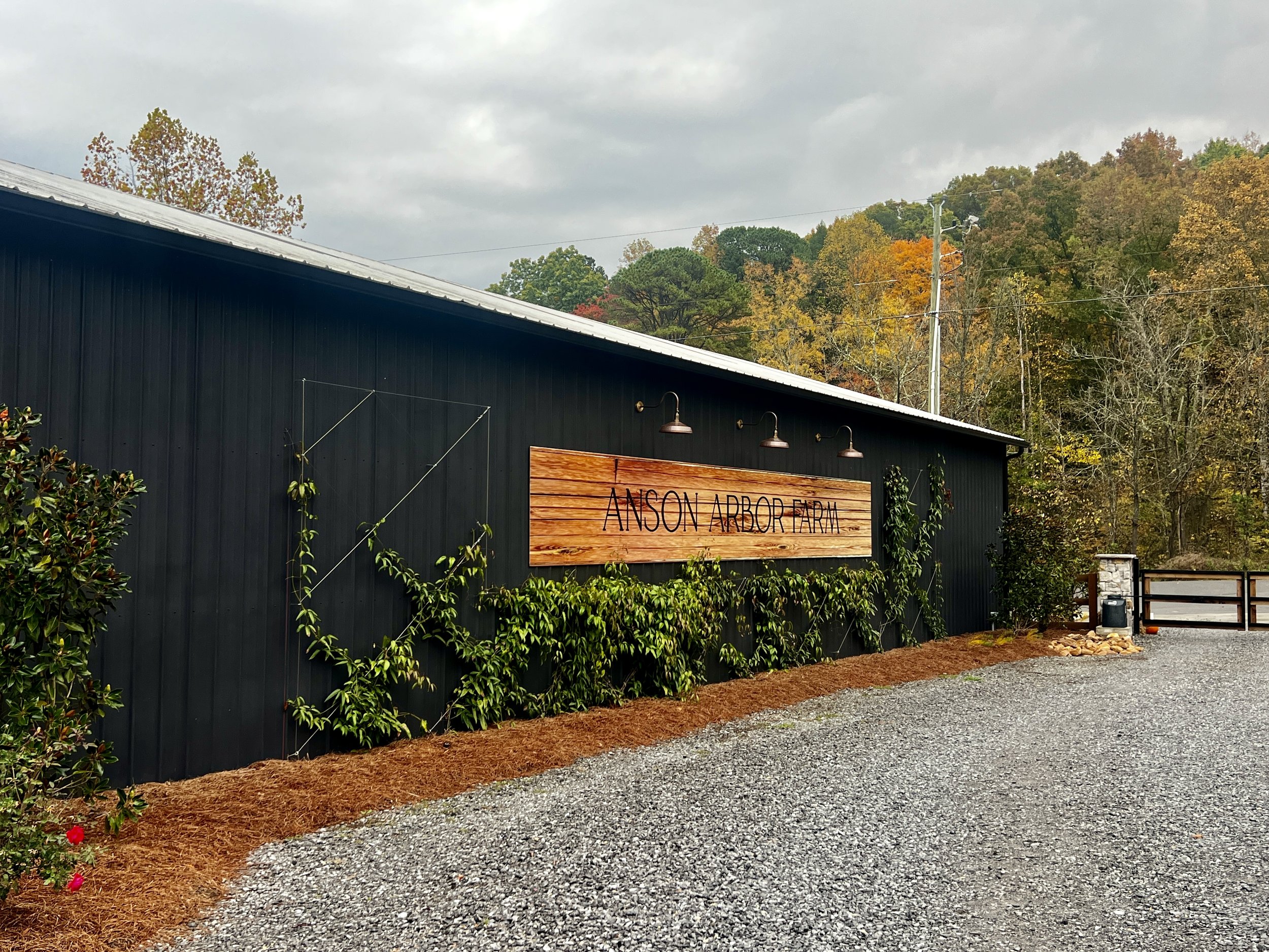 A black building with a sign reading "Anson Arbor Farm," surrounded by trees and greenery on a cloudy day.