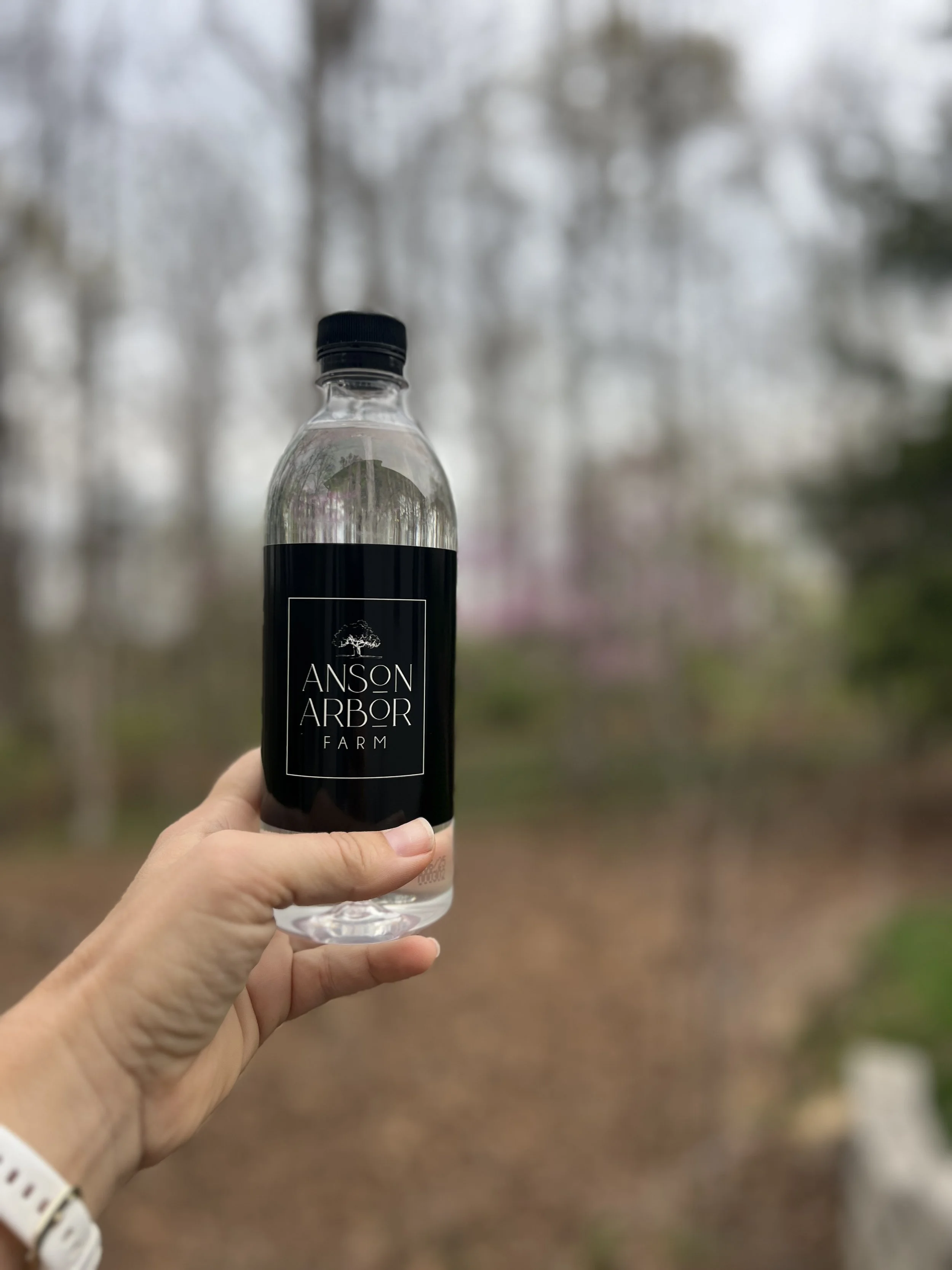 Person holding bottle labeled "Anson Arbor Farm" outdoors