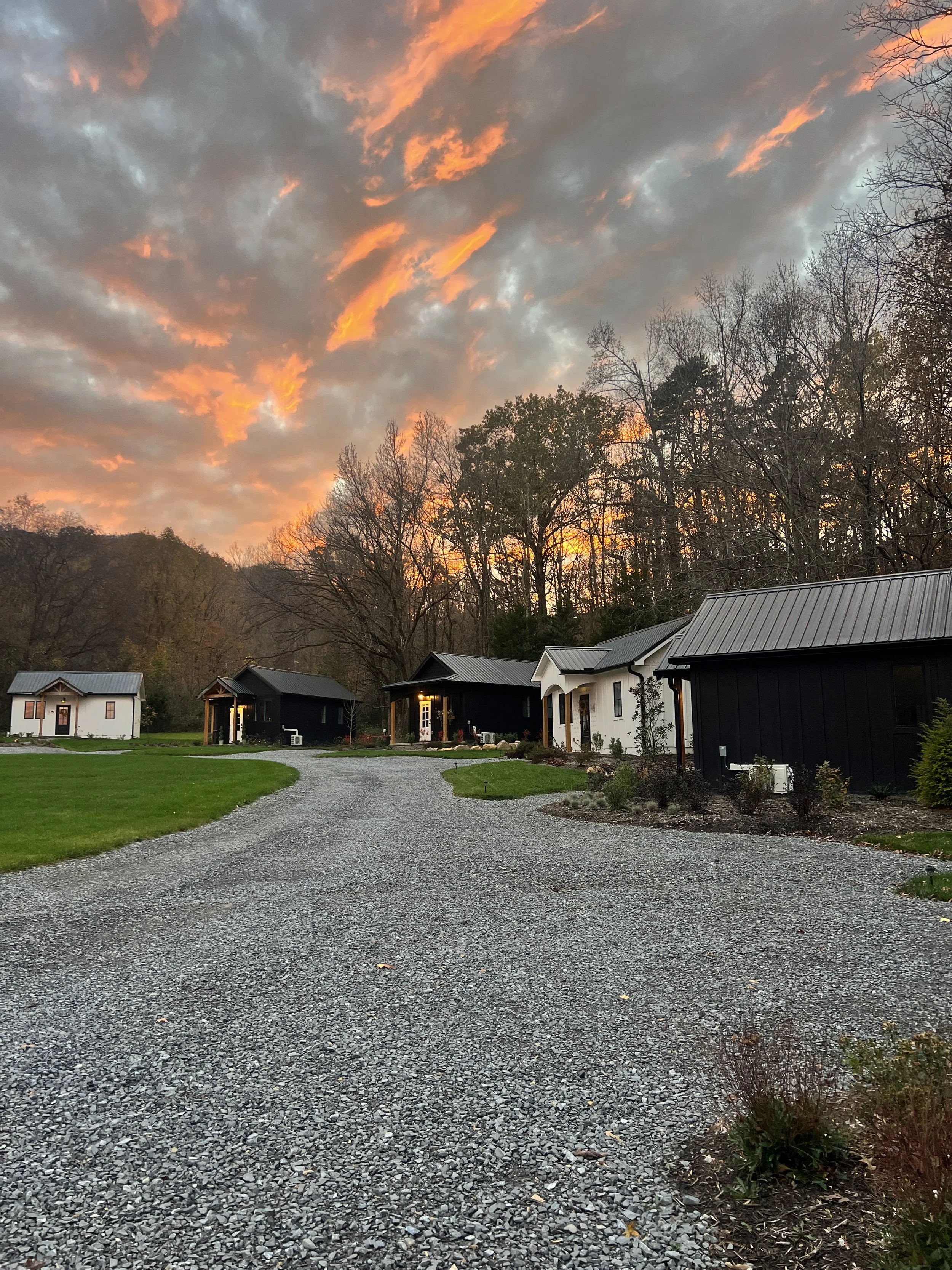 Gravel path leading to a row of small houses with a dramatic sunset sky above and trees in the background.