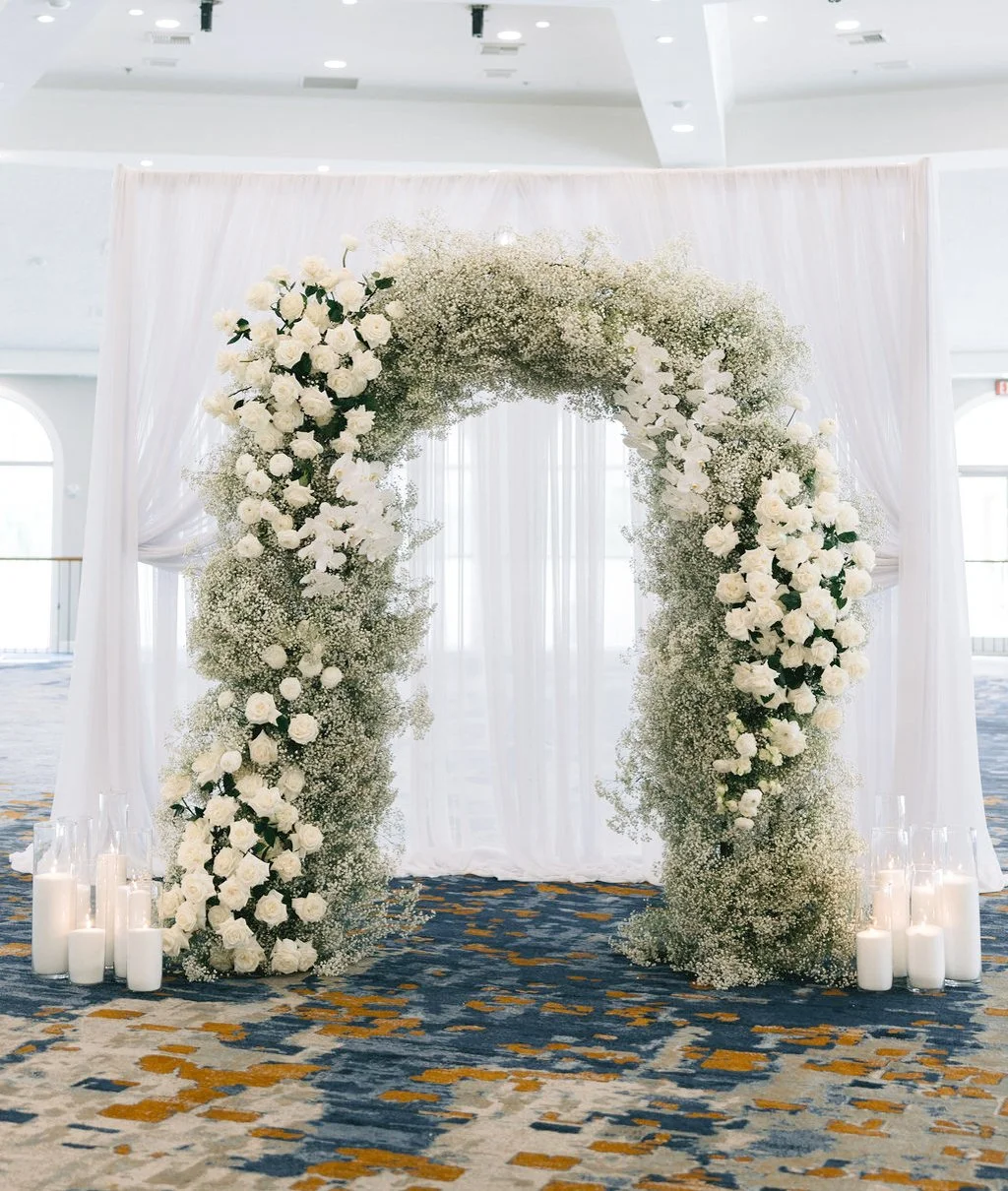 Full baby's breath and white rose wedding arch against white drapery with pillar candles, Las Vegas wedding florals