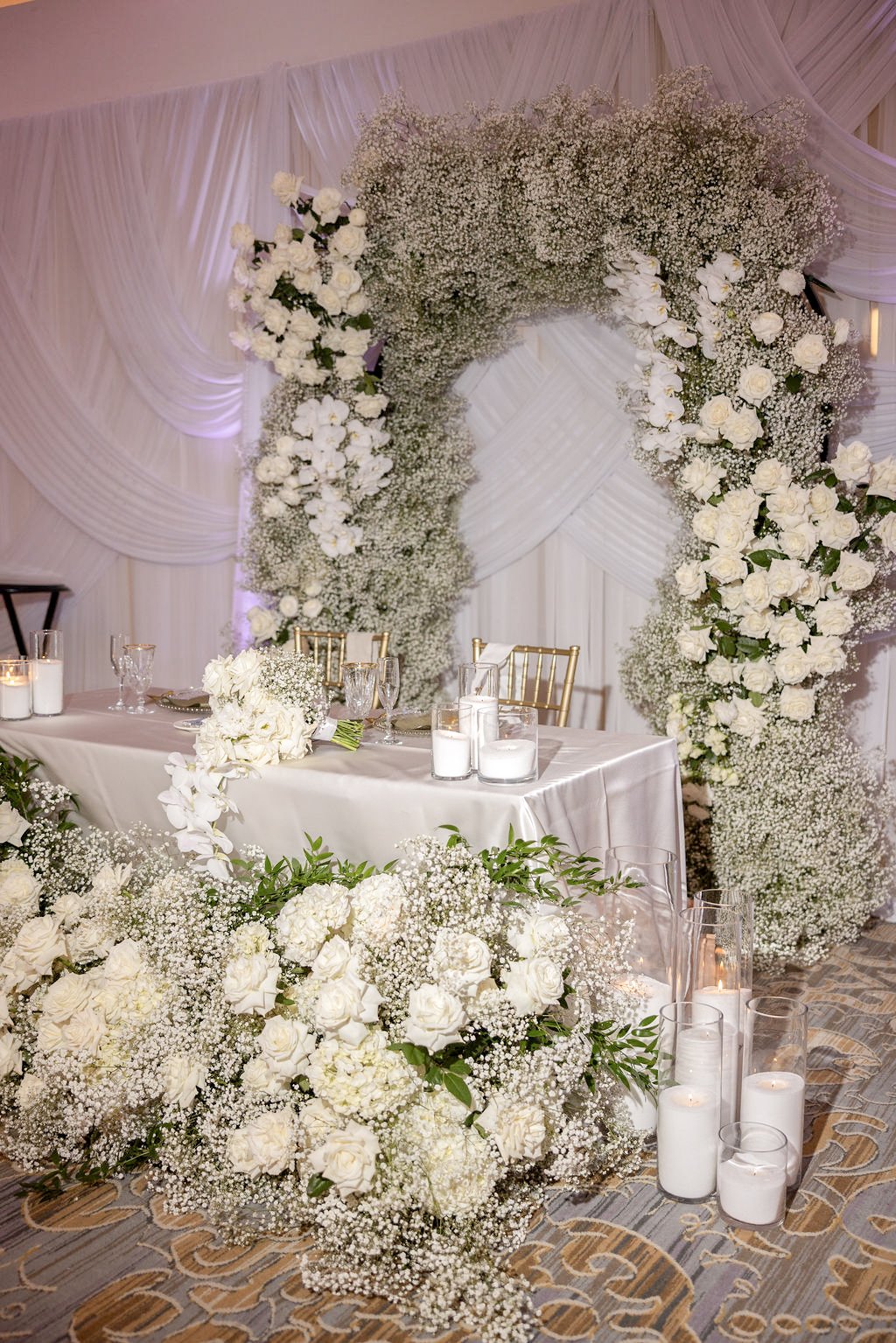 Sweetheart table framed by a baby's breath and white rose arch with cascading hydrangea garland, Las Vegas wedding floral installation