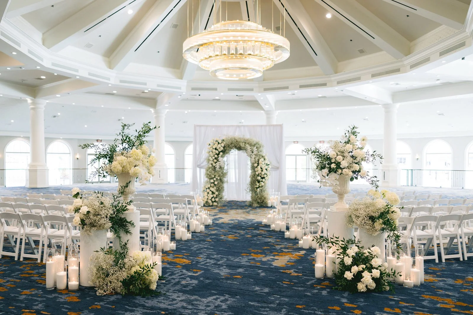 Ballroom ceremony with a baby's breath arch, draped backdrop and candlelit aisle designed by a Las Vegas wedding florist