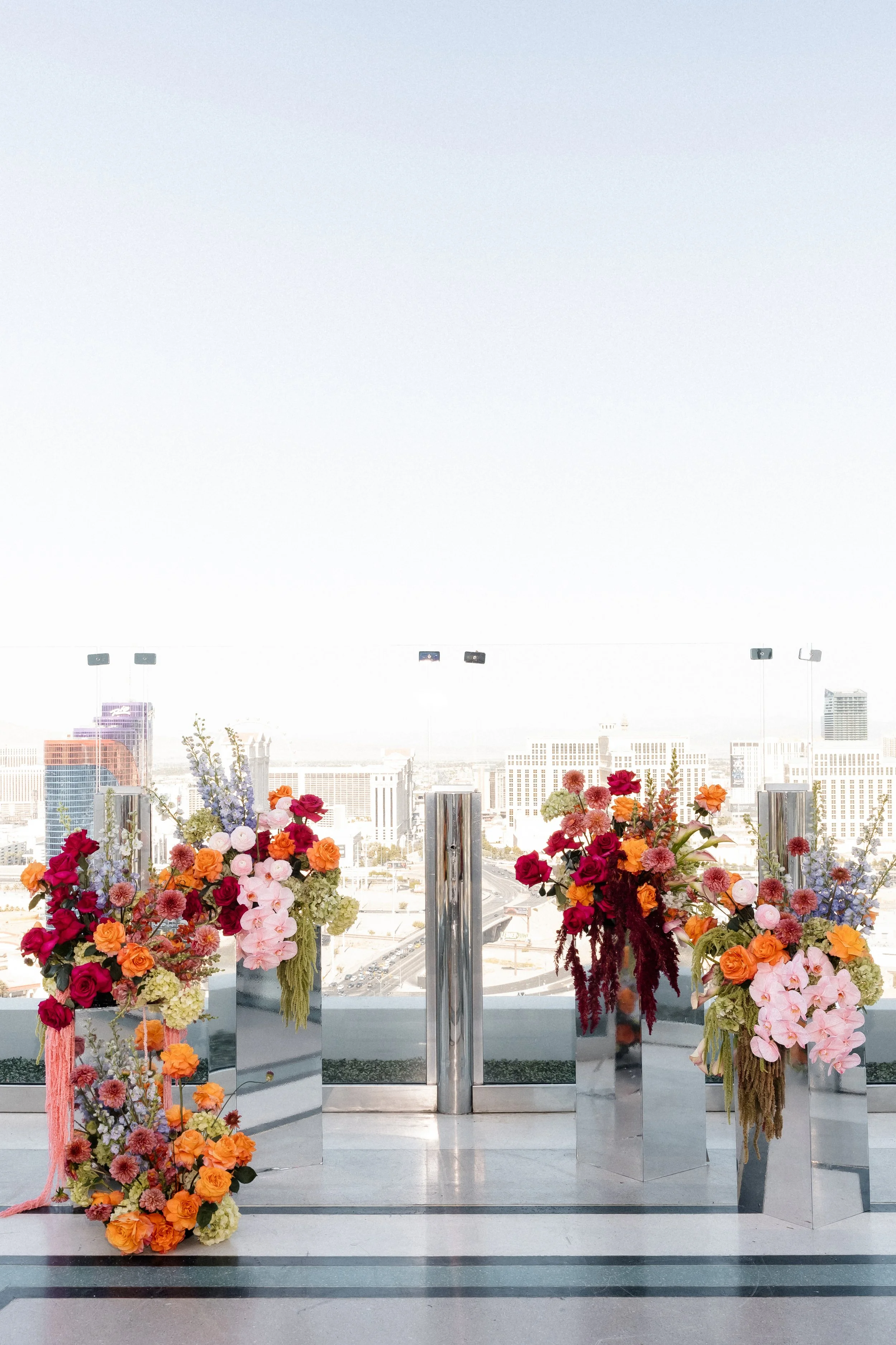 Rooftop ceremony above the Las Vegas Strip with mirrored plinths of magenta, coral and orange blooms and cascading pink amaranthus, Las Vegas wedding florist