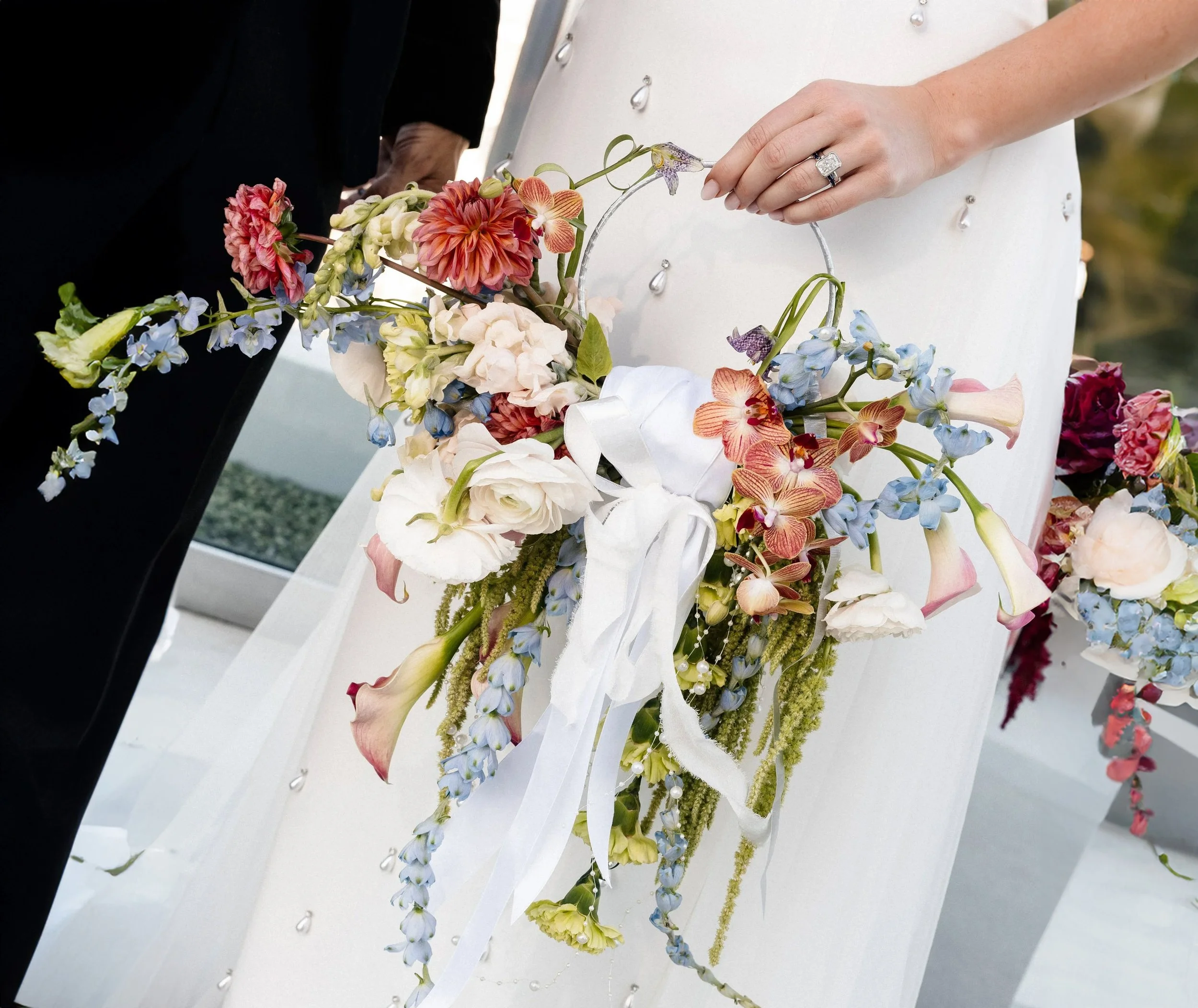 Bride holding a crescent hoop bouquet of dahlias, orchids, ranunculus and trailing amaranthus tied with white silk ribbon, Las Vegas elopement florals