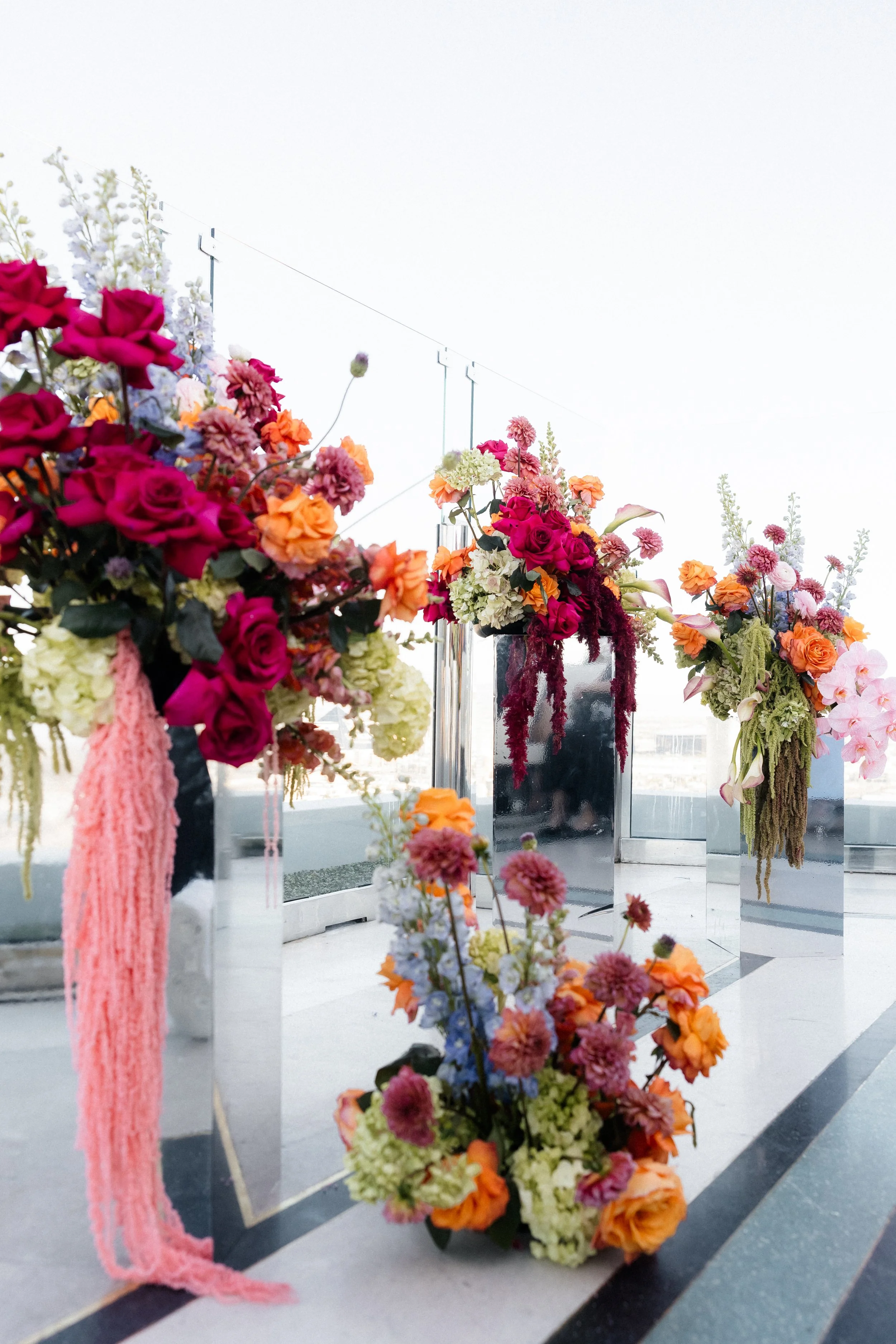 Mirrored pedestal arrangements in fuchsia roses, delphinium and hanging pink amaranthus at a Las Vegas rooftop wedding ceremony
