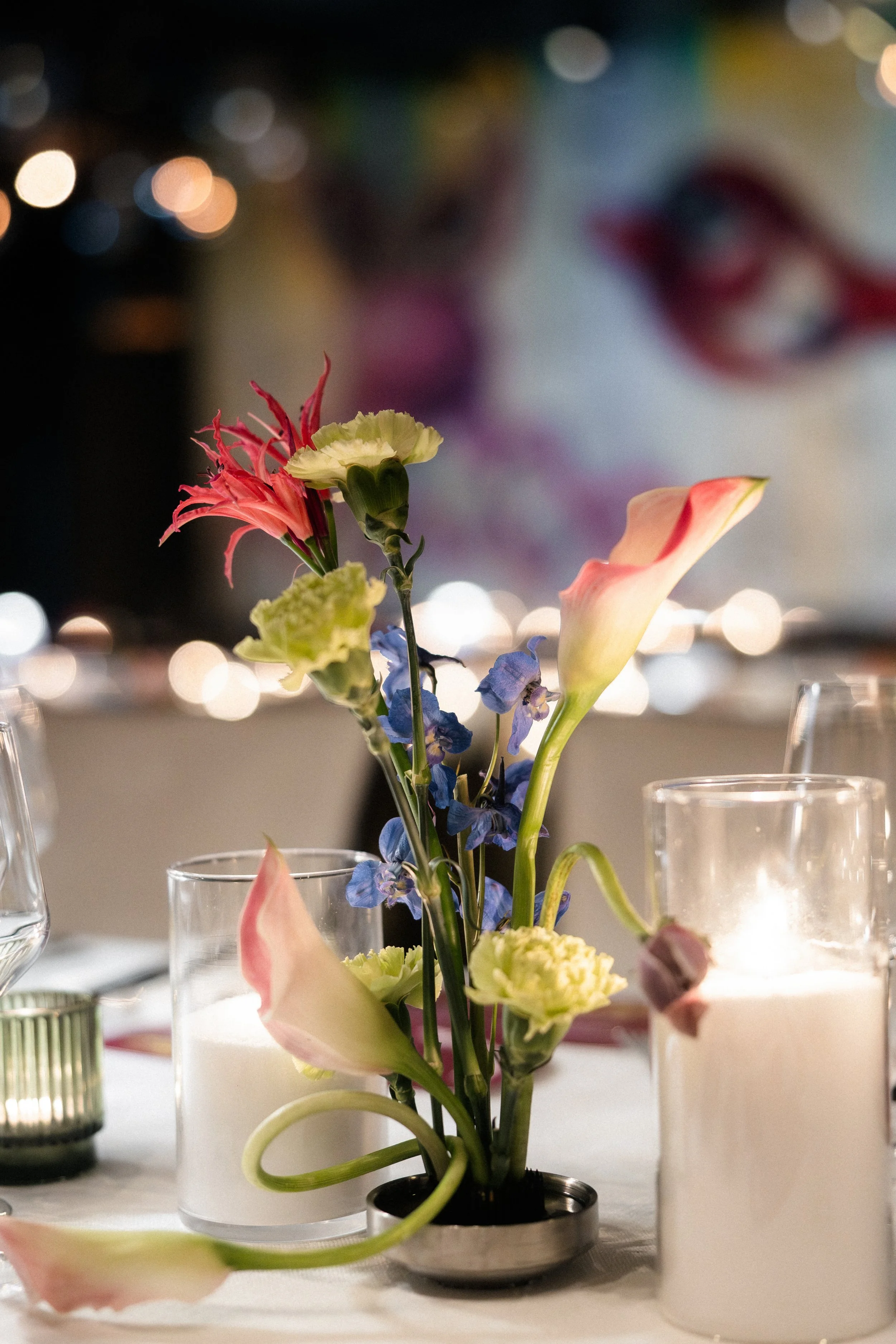 Candlelit reception centerpiece with peach calla lilies, green carnations and blue delphinium in glass vessels, Las Vegas wedding florist reception design