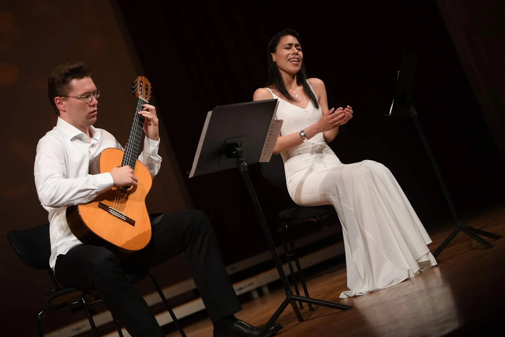 A man playing guitar and a woman singing during a musical performance on stage.