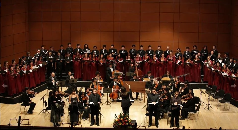 A large choir performing with multiple musicians and a conductor on stage