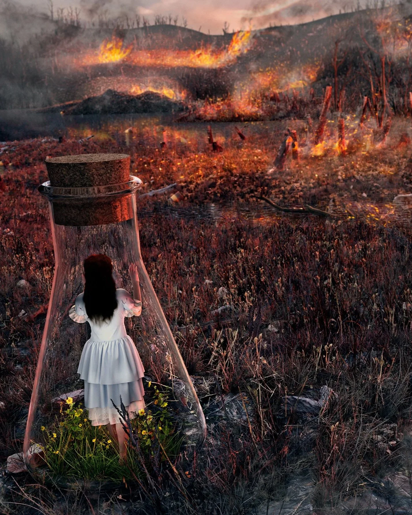A woman in a white dress is standing in a field of grass and flowers, looking at a forest fire burning in the distance with large flames and smoke rising in the sky.