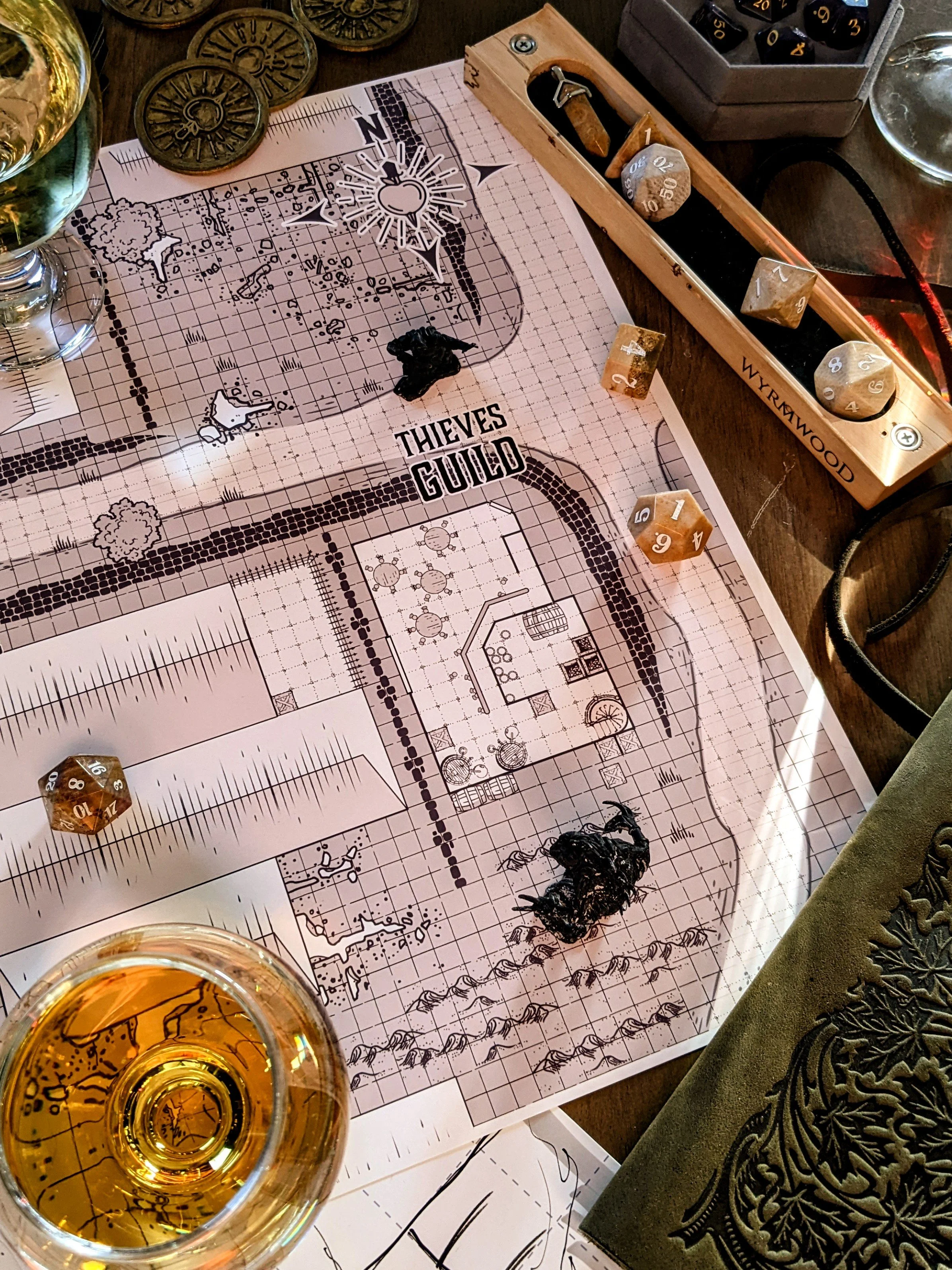 A Picture of a thieves guild designed DND layout. Surrounded by a glass of sider and 20 sided dice.