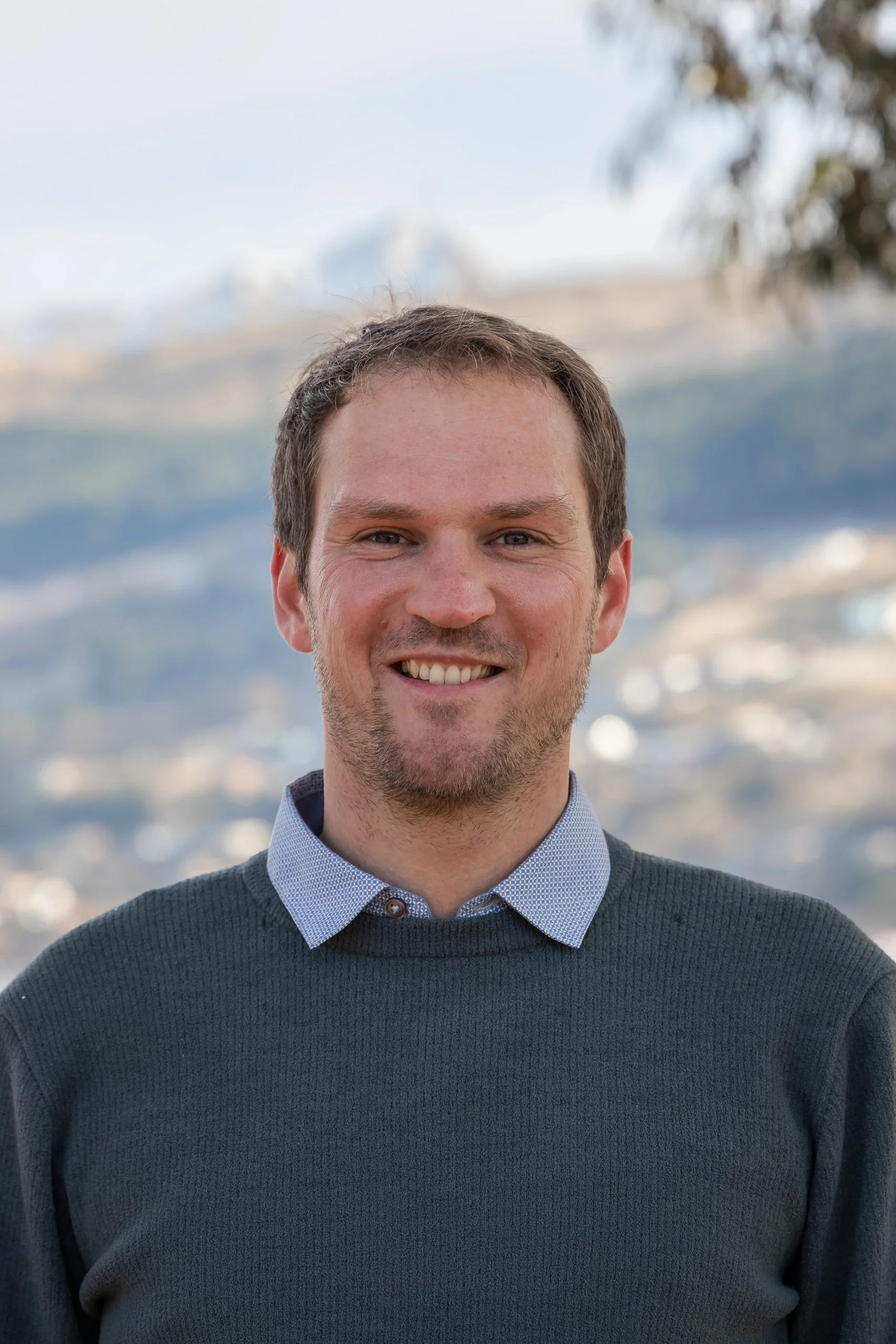 Portrait of a smiling man outdoors with mountains in the background.