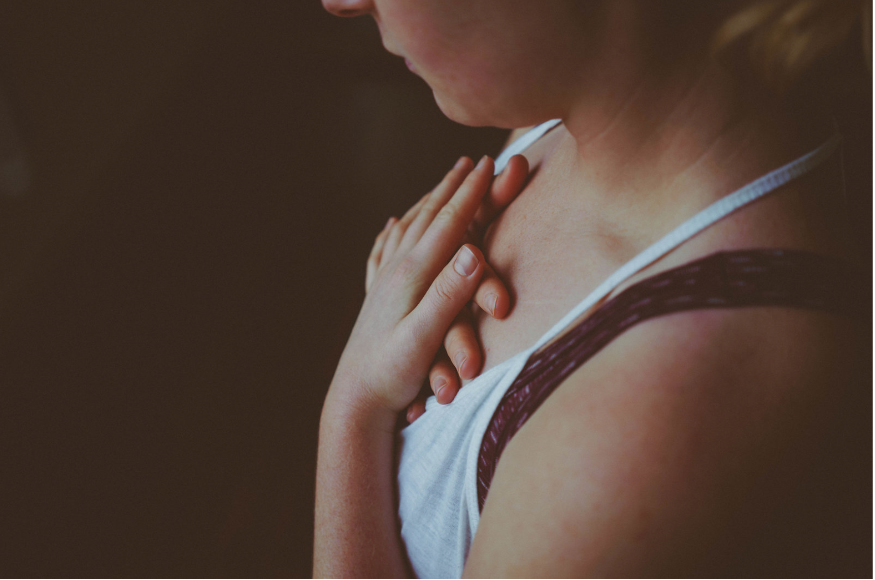 A woman touches her chest with both hands in a gesture that suggests she is experiencing chest pain or discomfort.