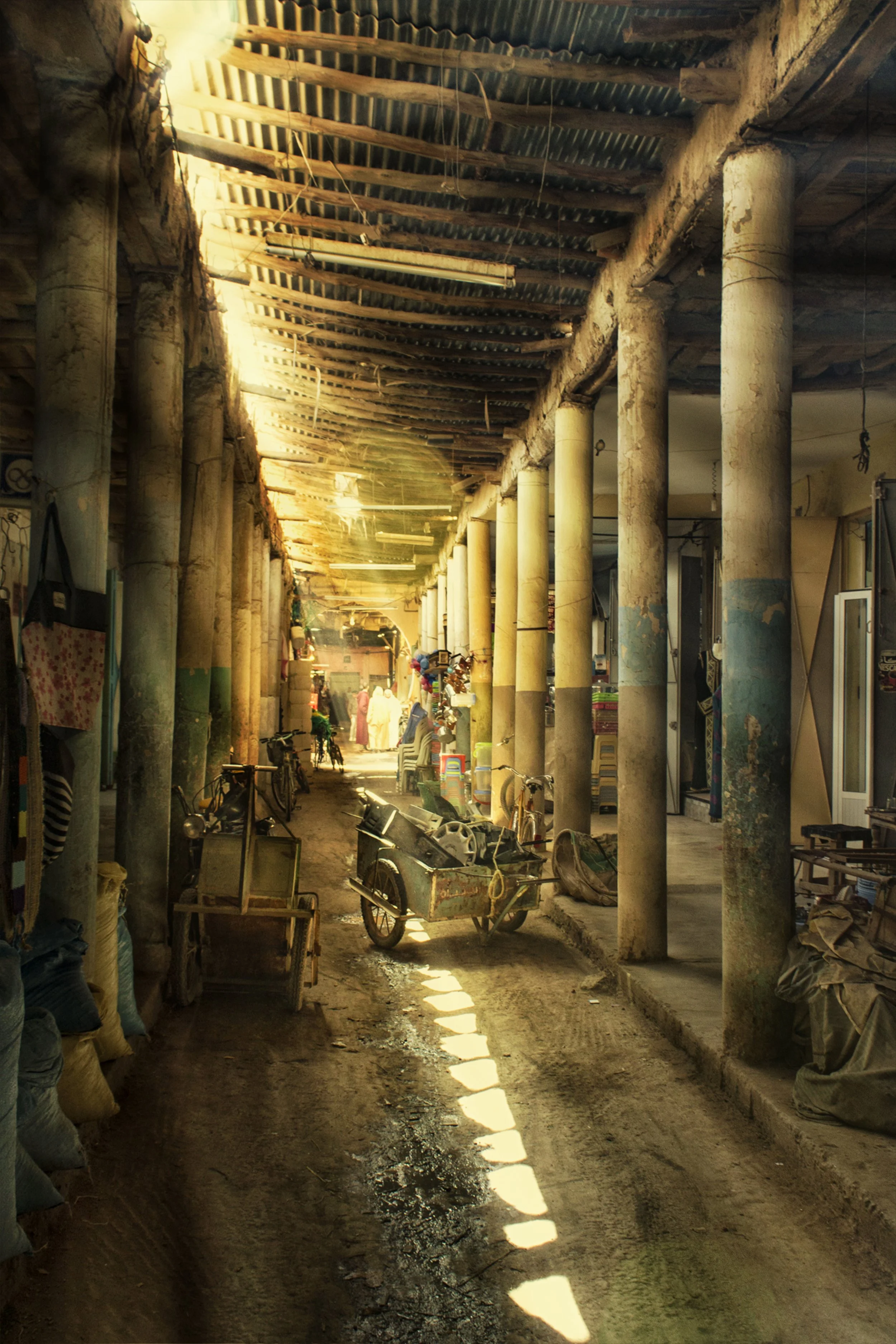 Photo by Kim Stone in Morocco. A narrow alleyway in a market with large concrete columns supporting a corrugated metal roof. 