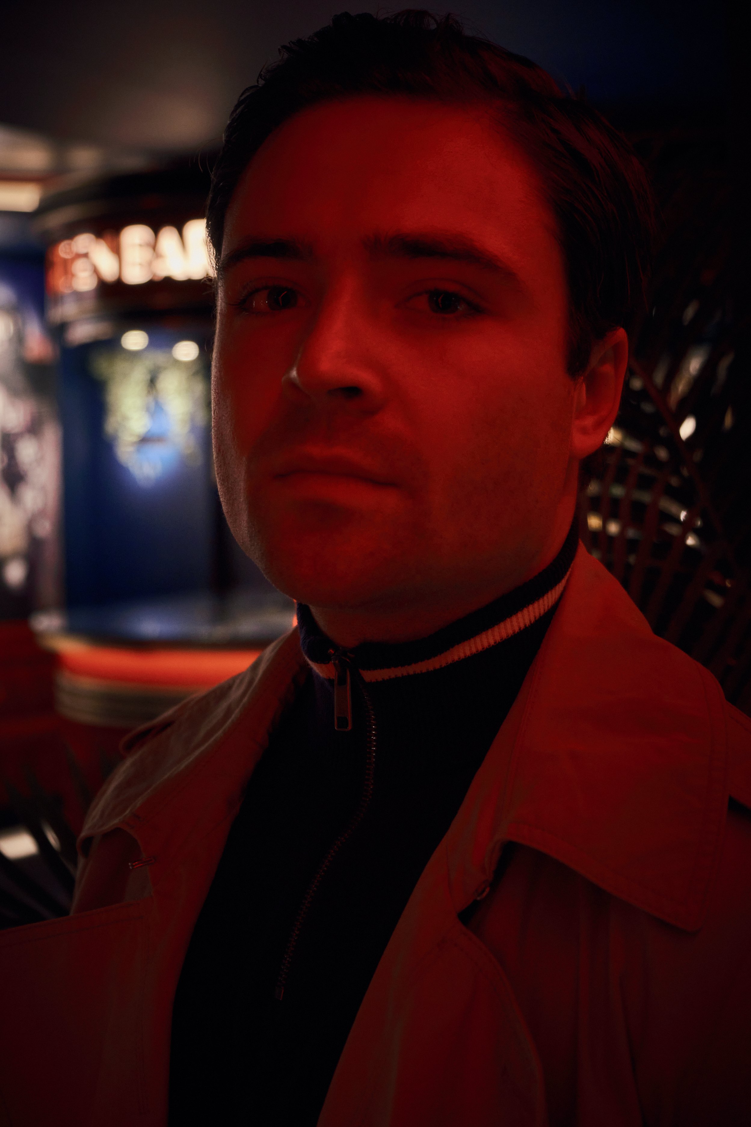 Person with red lighting and serious expression in dimly lit room.