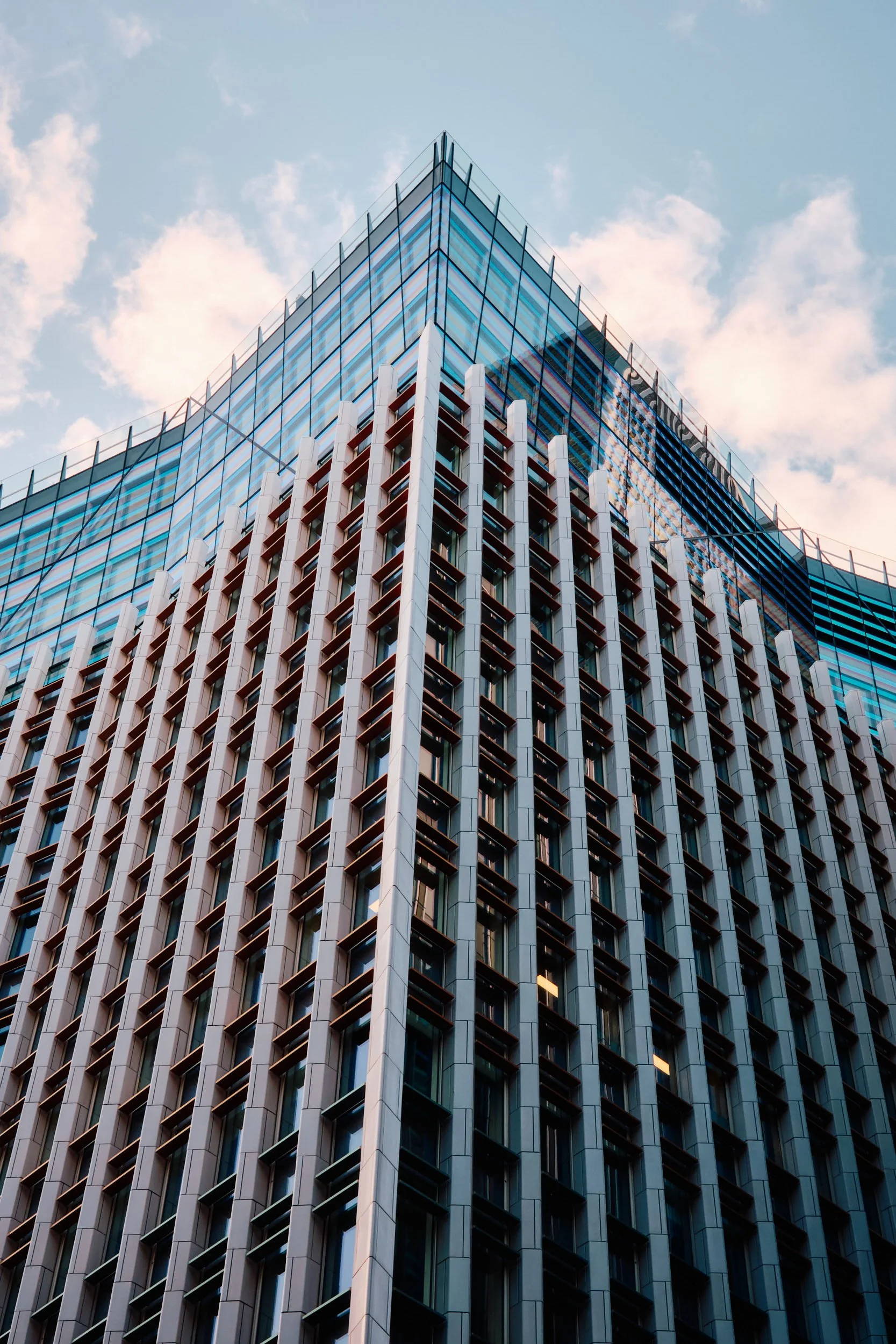 Modern glass skyscraper with a grid-like facade against a blue sky with clouds
