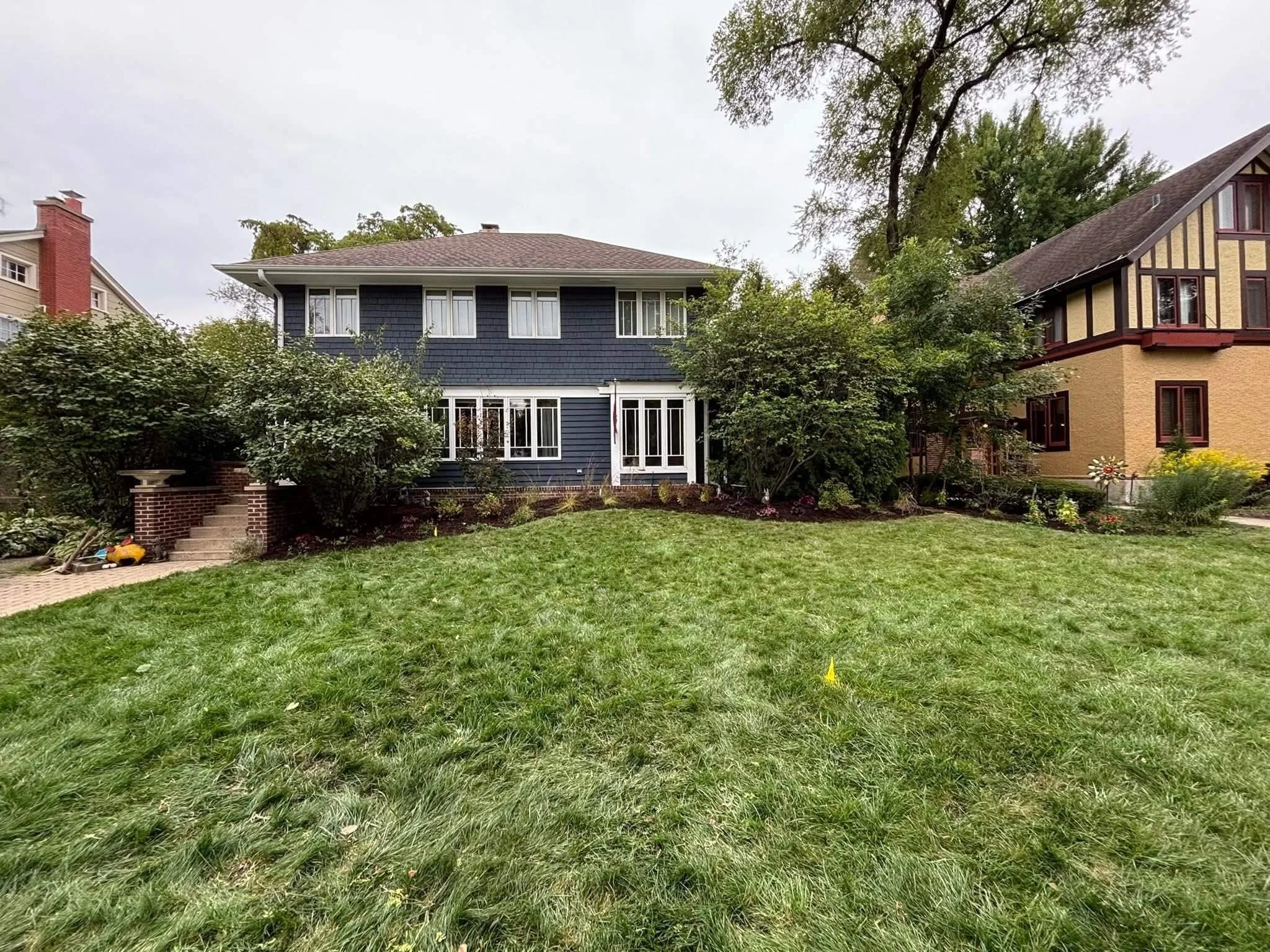 Wide view of Chicago front yard after native garden installation with defined planting beds, lawn area, and restored historic home visibility